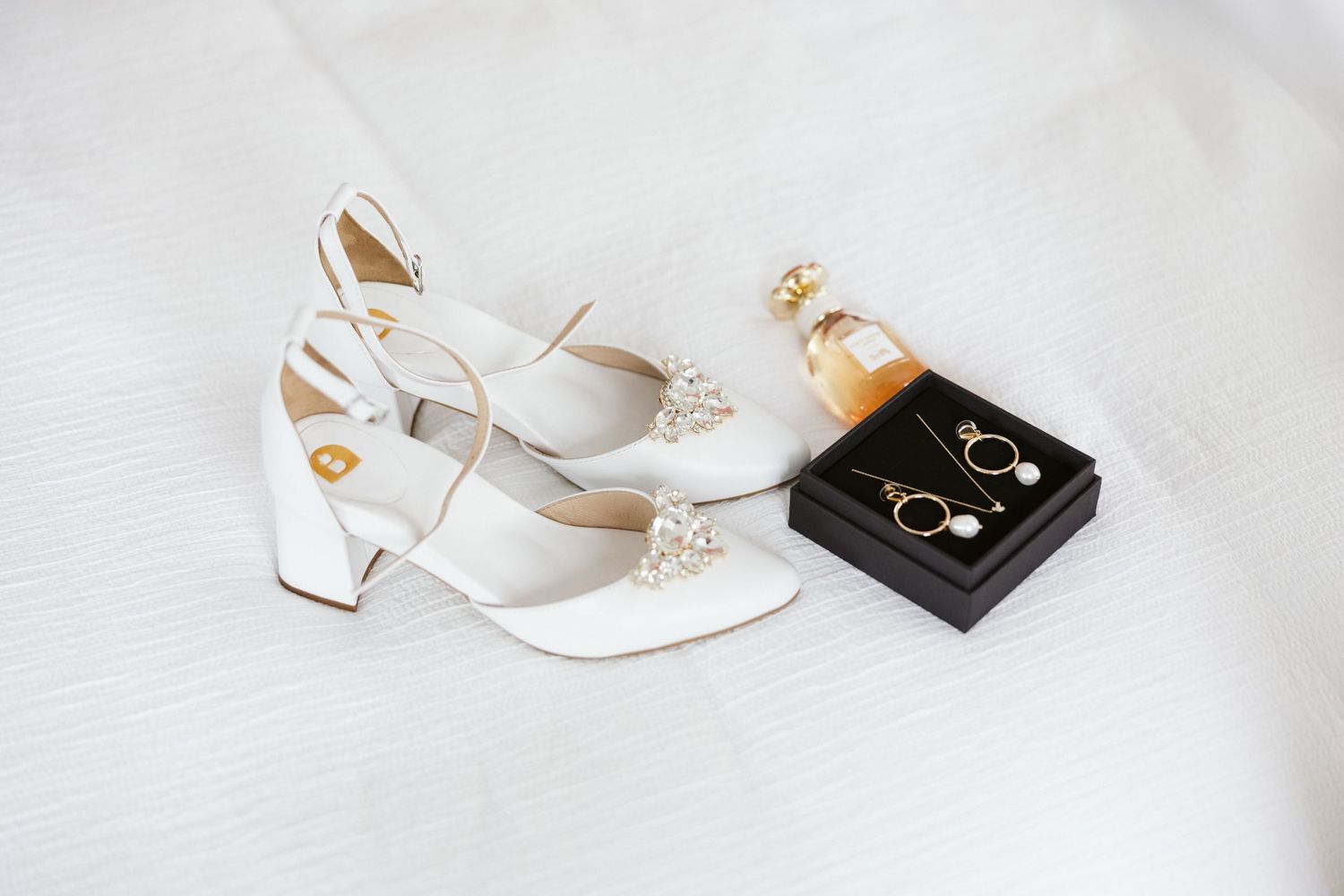 White bridal shoes and jewelry box arranged on white fabric.