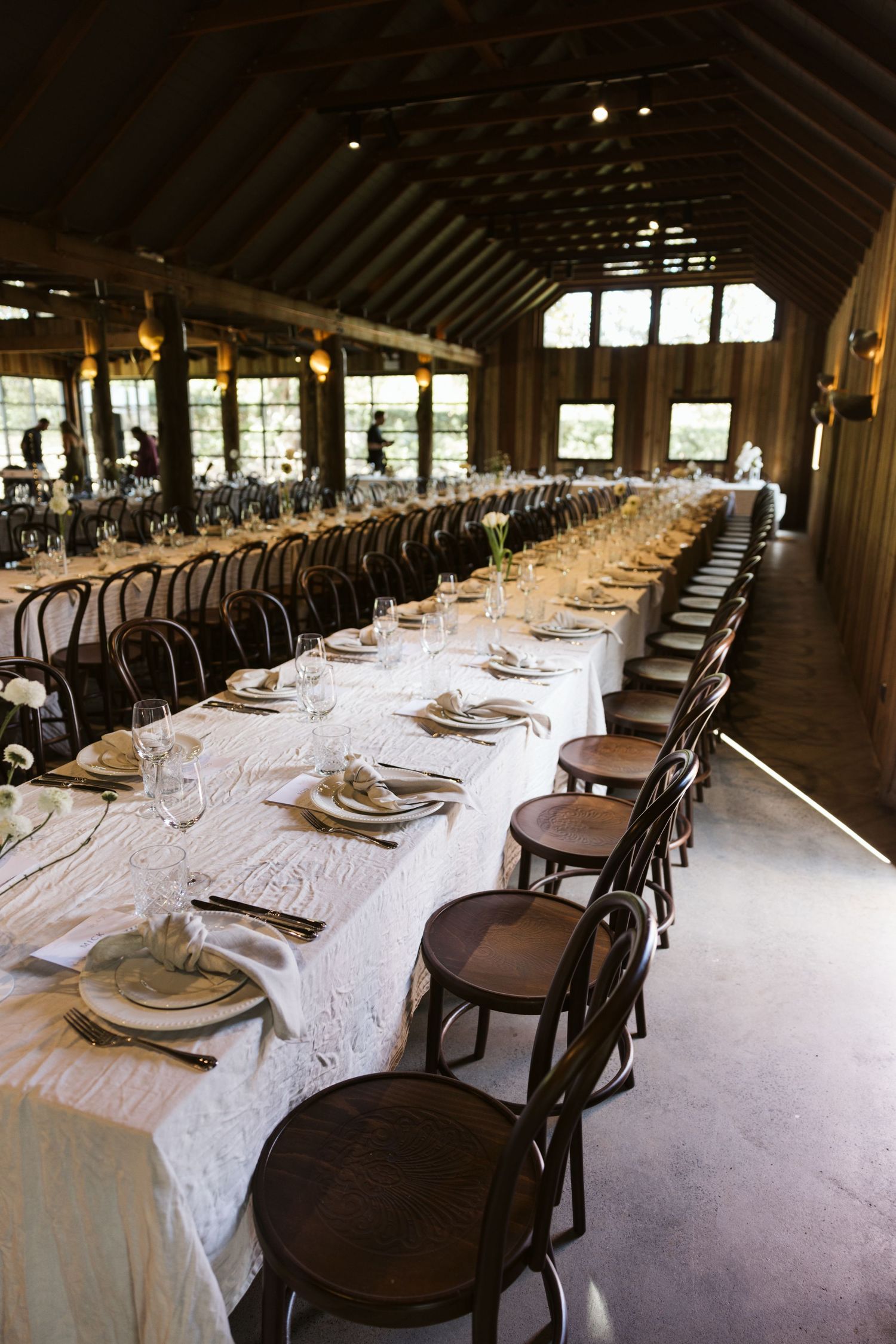 Long banquet table with elegant place settings and bentwood chairs in rustic wooden event venue.