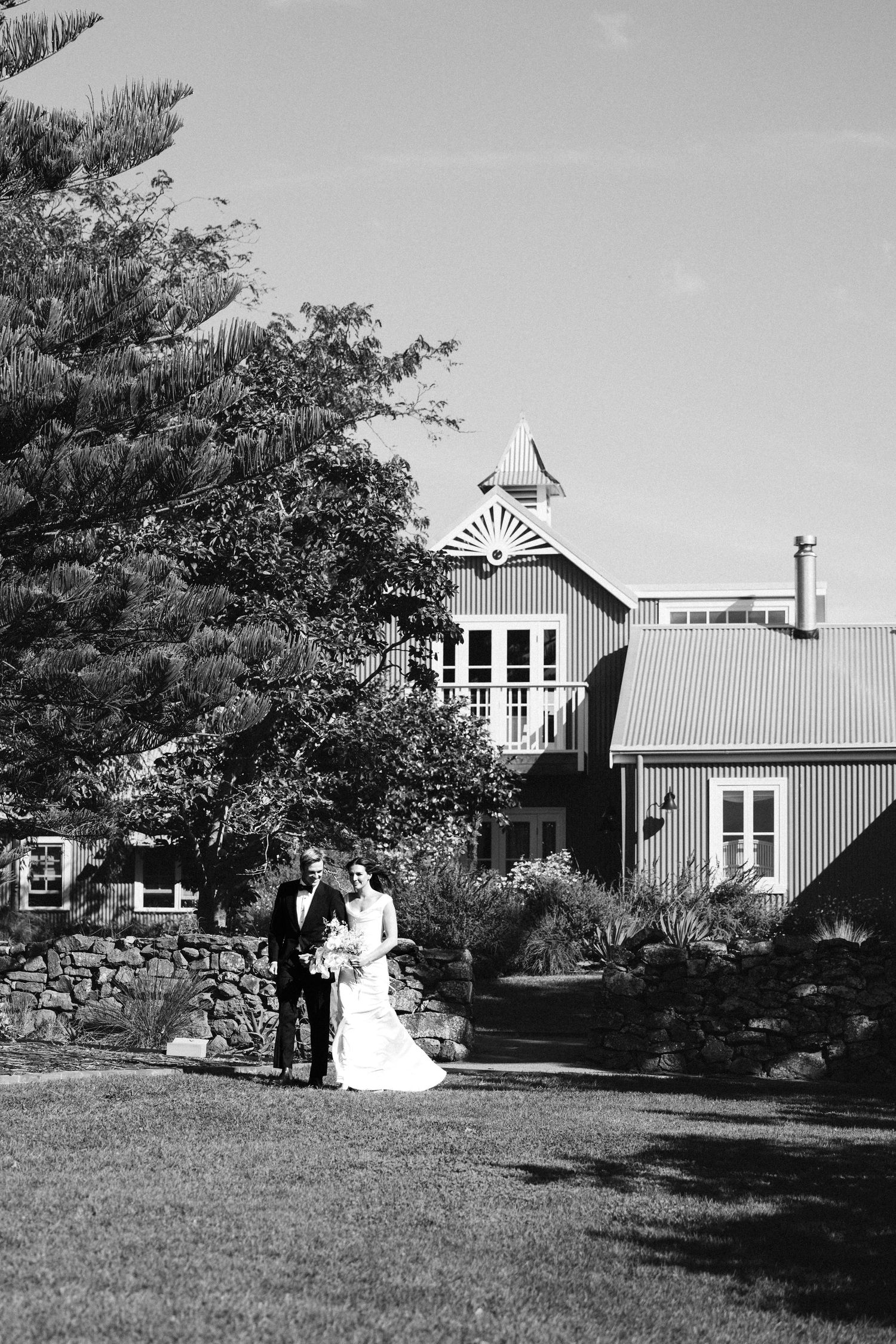 Black and white photo of a wedding ceremony at a rustic venue with a stone wall and tall trees.