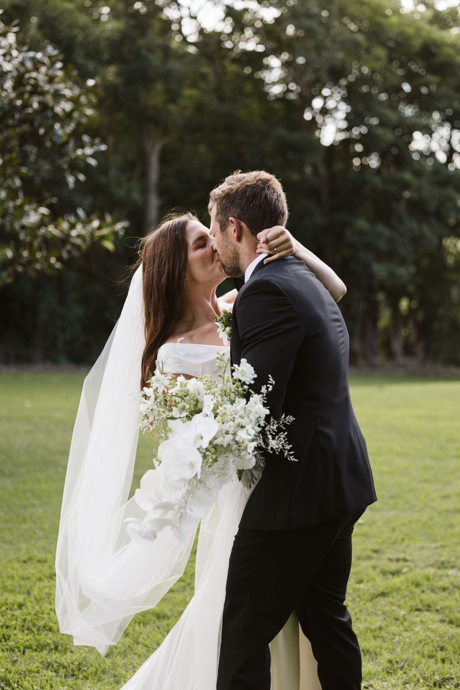 Romantic wedding portrait with flowing veil and white bouquet in garden setting.