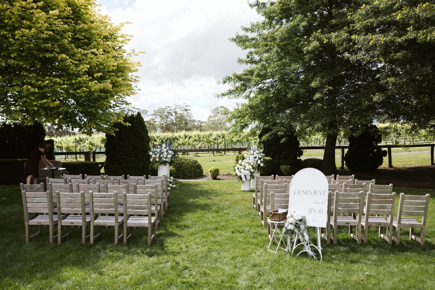 White wooden chairs arranged for an outdoor wedding ceremony on a manicured lawn.