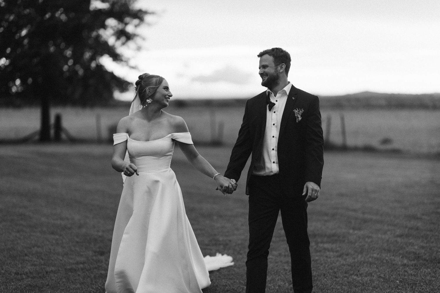 Black and white portrait of couple walking and laughing together on grass field.
