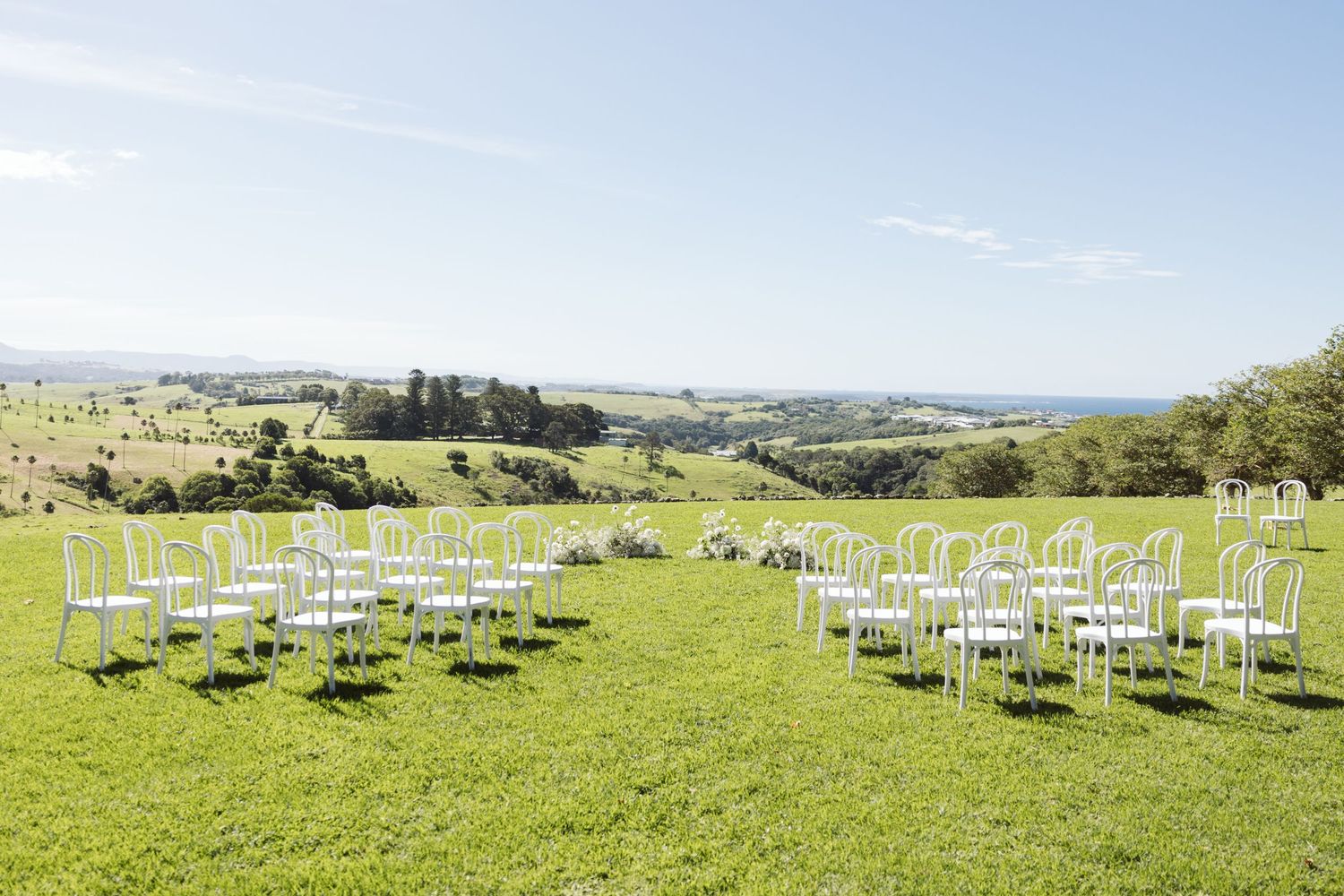White chairs arranged on a hillside lawn for an outdoor wedding ceremony with scenic countryside views.