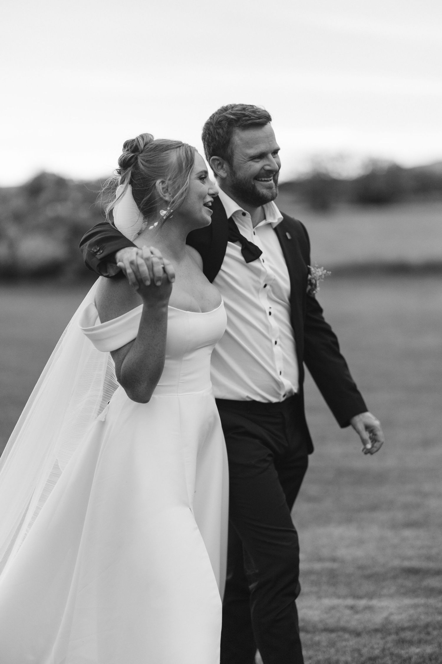 A candid black and white photo captures a joyful moment between newlyweds outdoors.