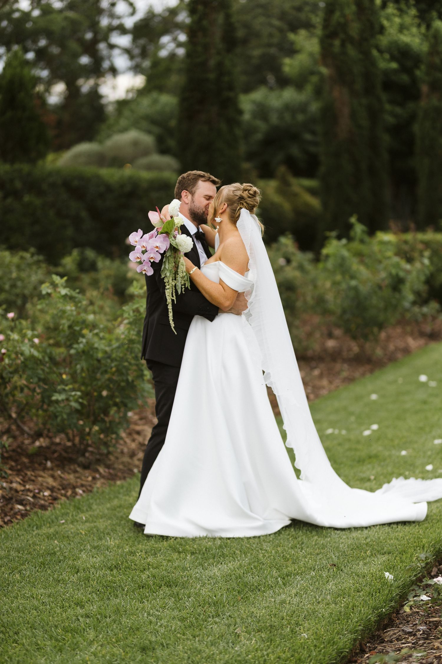 A romantic wedding kiss moment captured in a garden setting with flowing white dress.