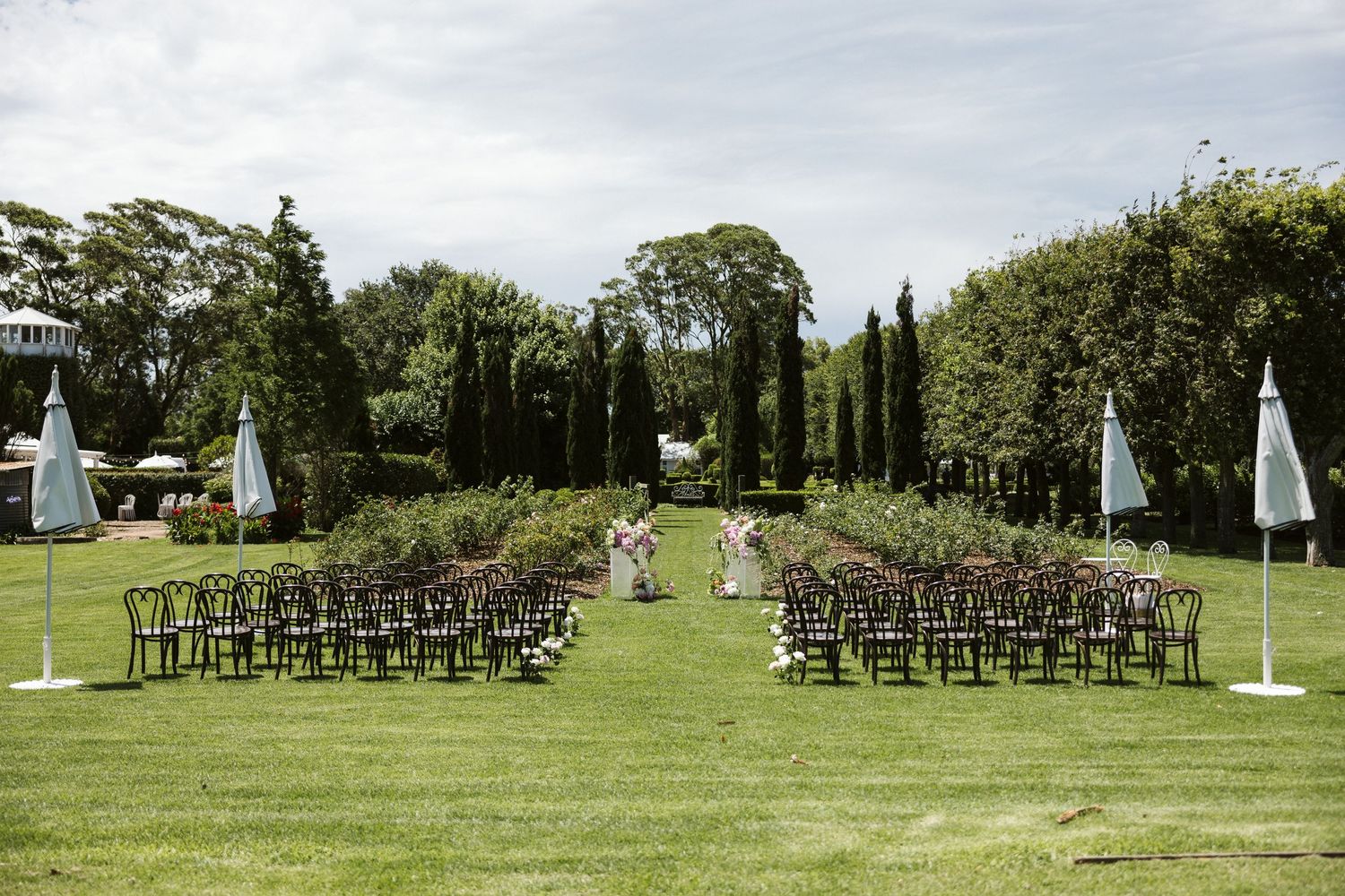 A symmetrical outdoor wedding venue with rows of chairs and cypress trees lining the aisle.