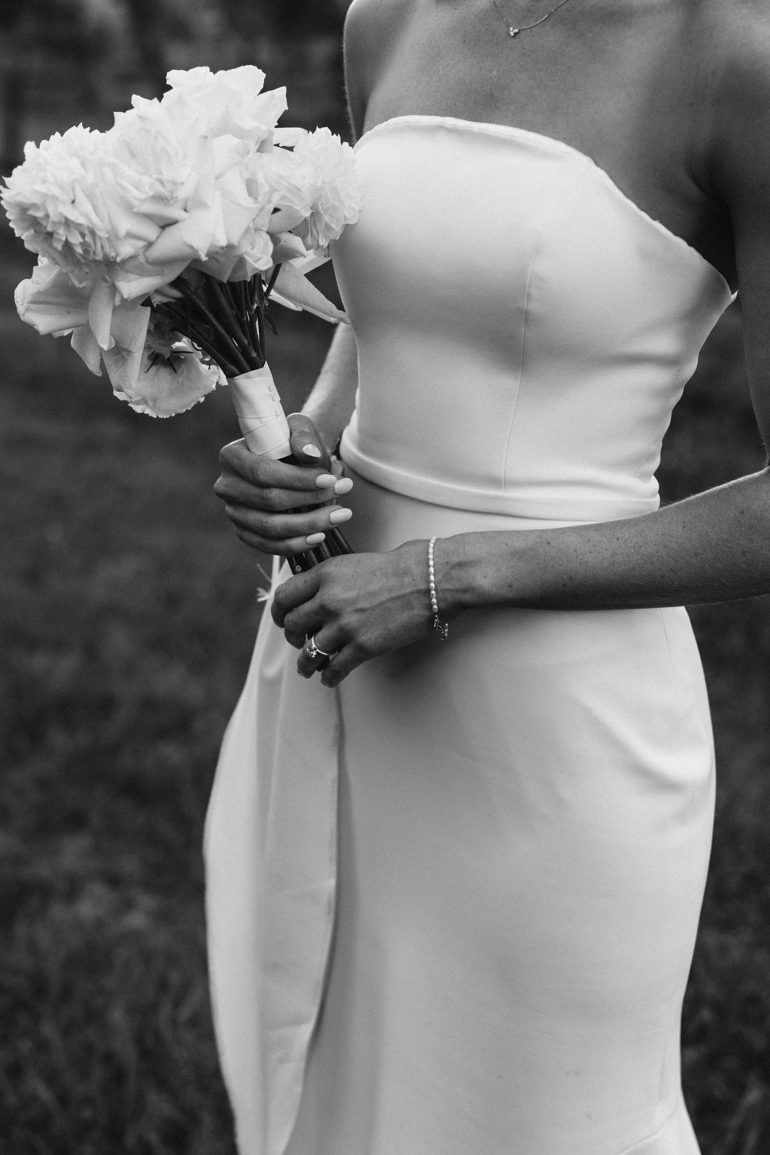 Close-up of bride holding white peony bouquet in elegant strapless wedding dress.