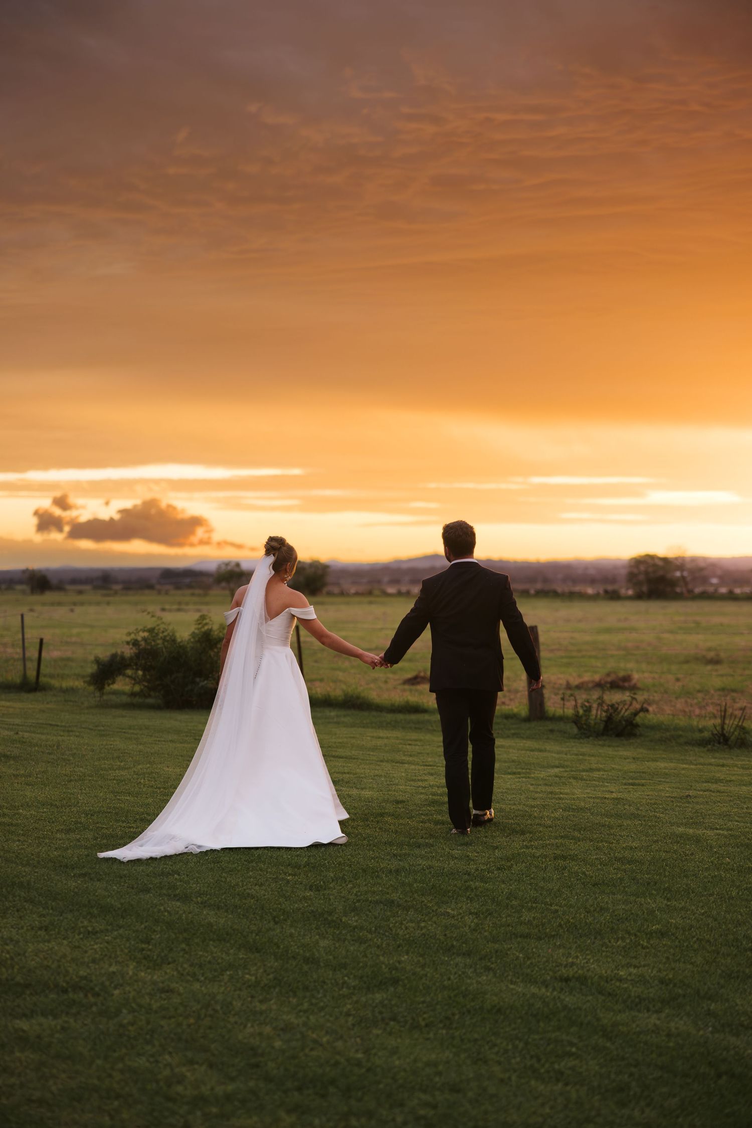Couple walking hand in hand across lawn during golden hour sunset.