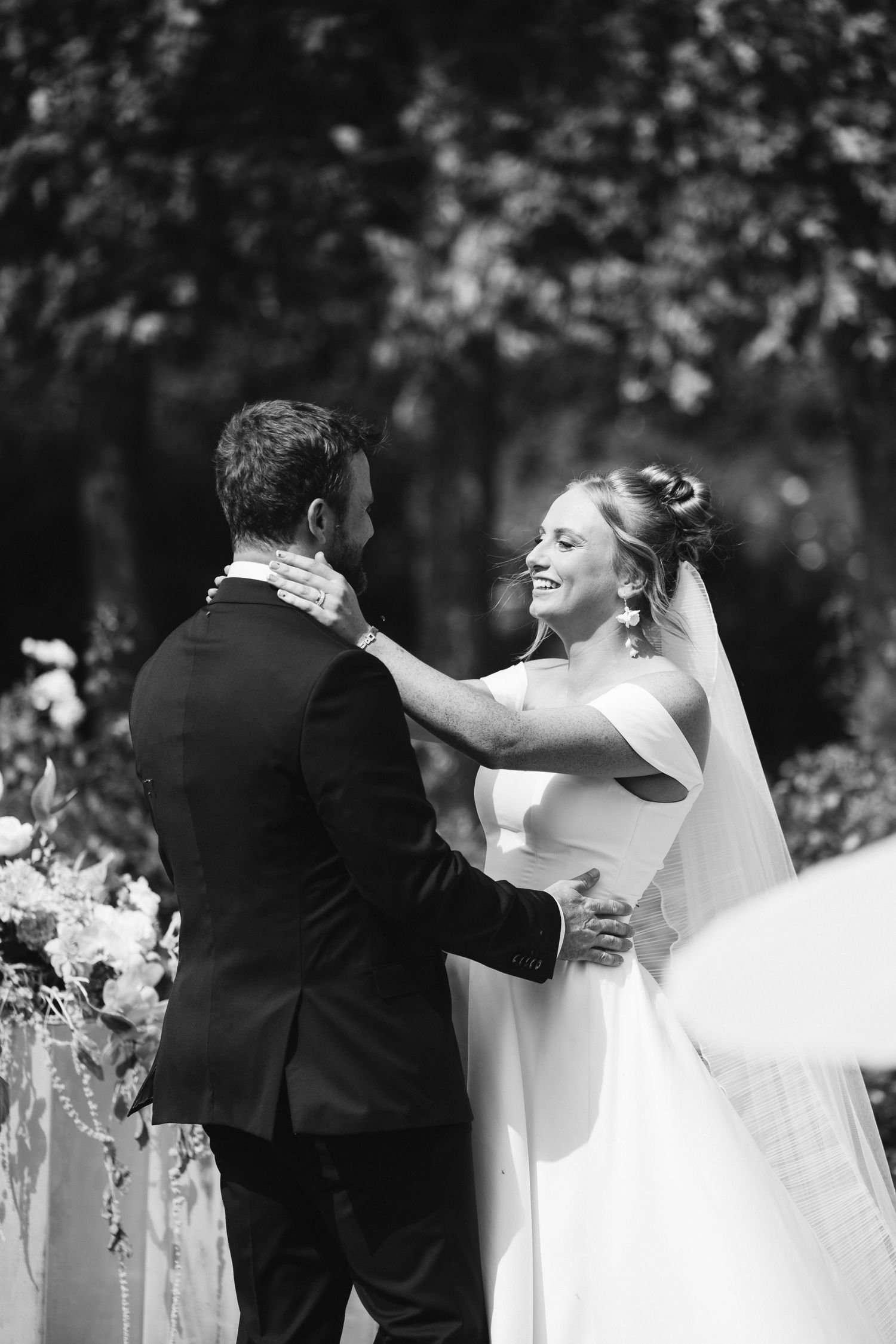 Black and white portrait of newlyweds embracing during outdoor ceremony.