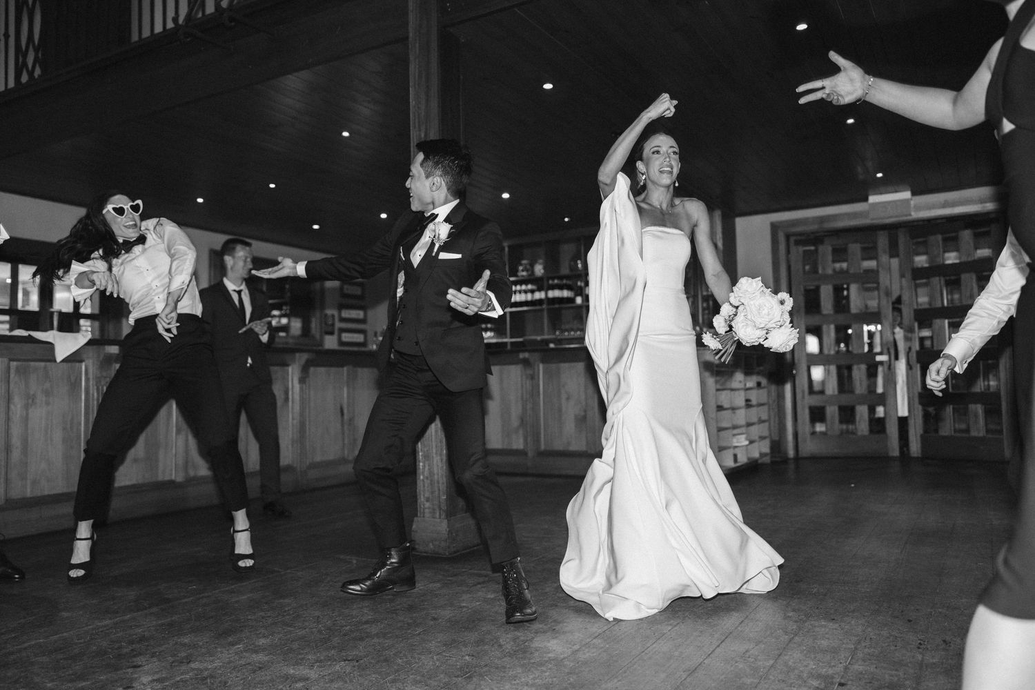 Black and white photo of energetic wedding dance party in rustic indoor venue.