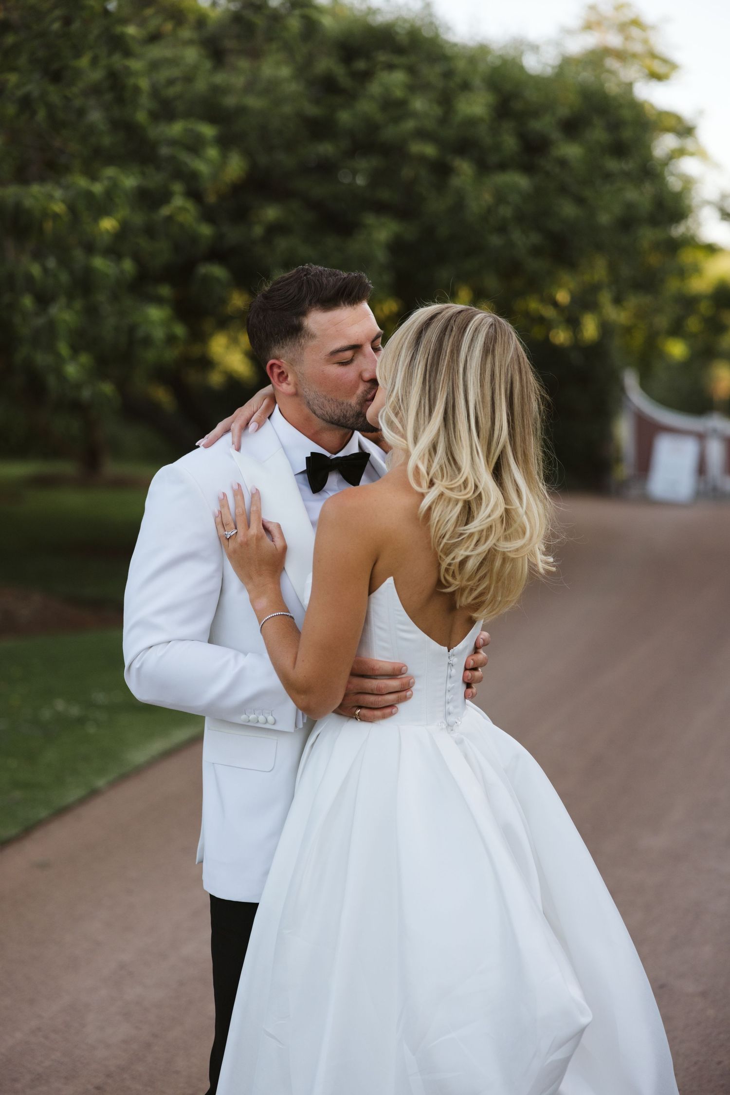 Romantic moment between bride and groom in white attire on garden path.