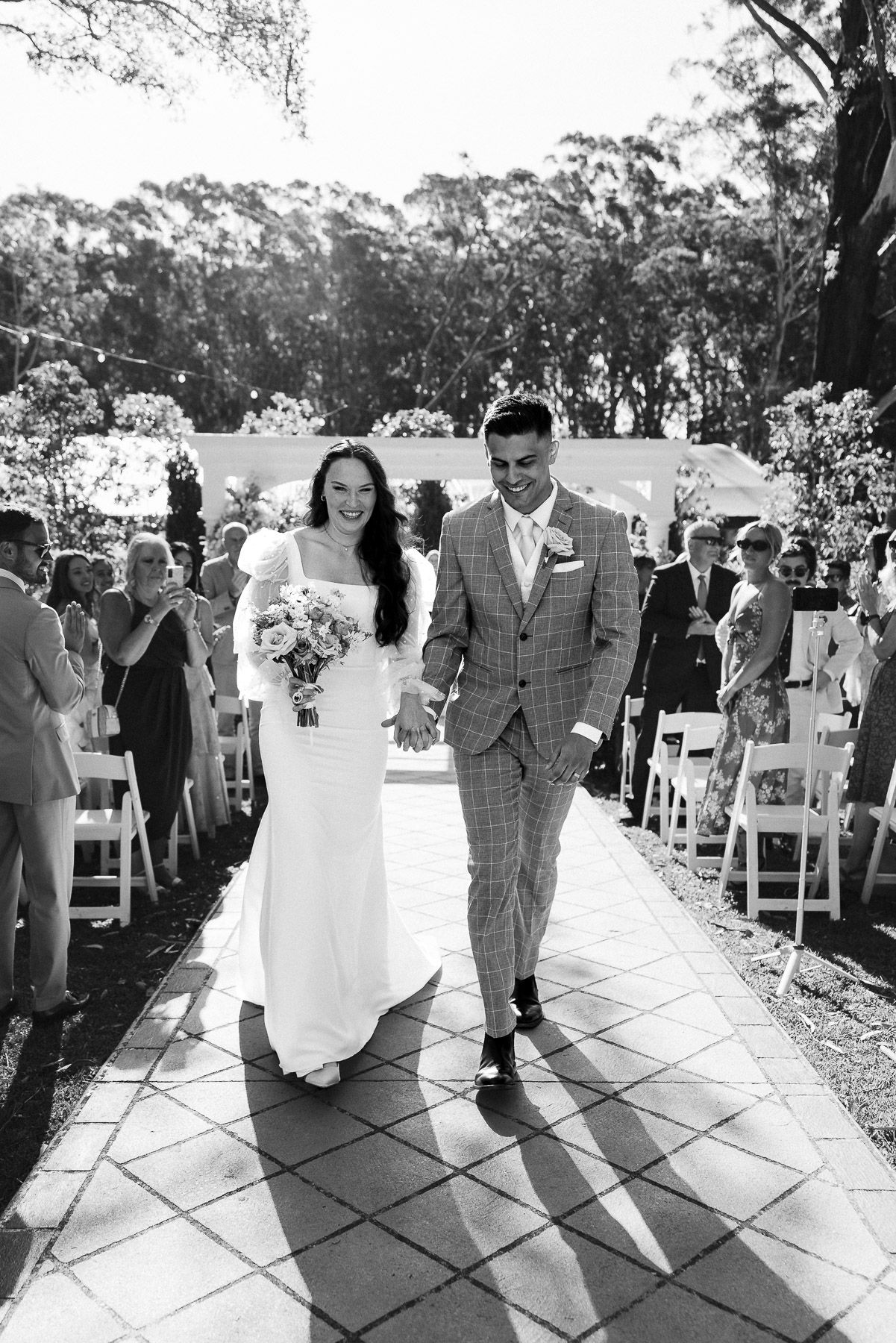 Black and white photo of a bride and groom walking down the aisle after their outdoor wedding ceremony.