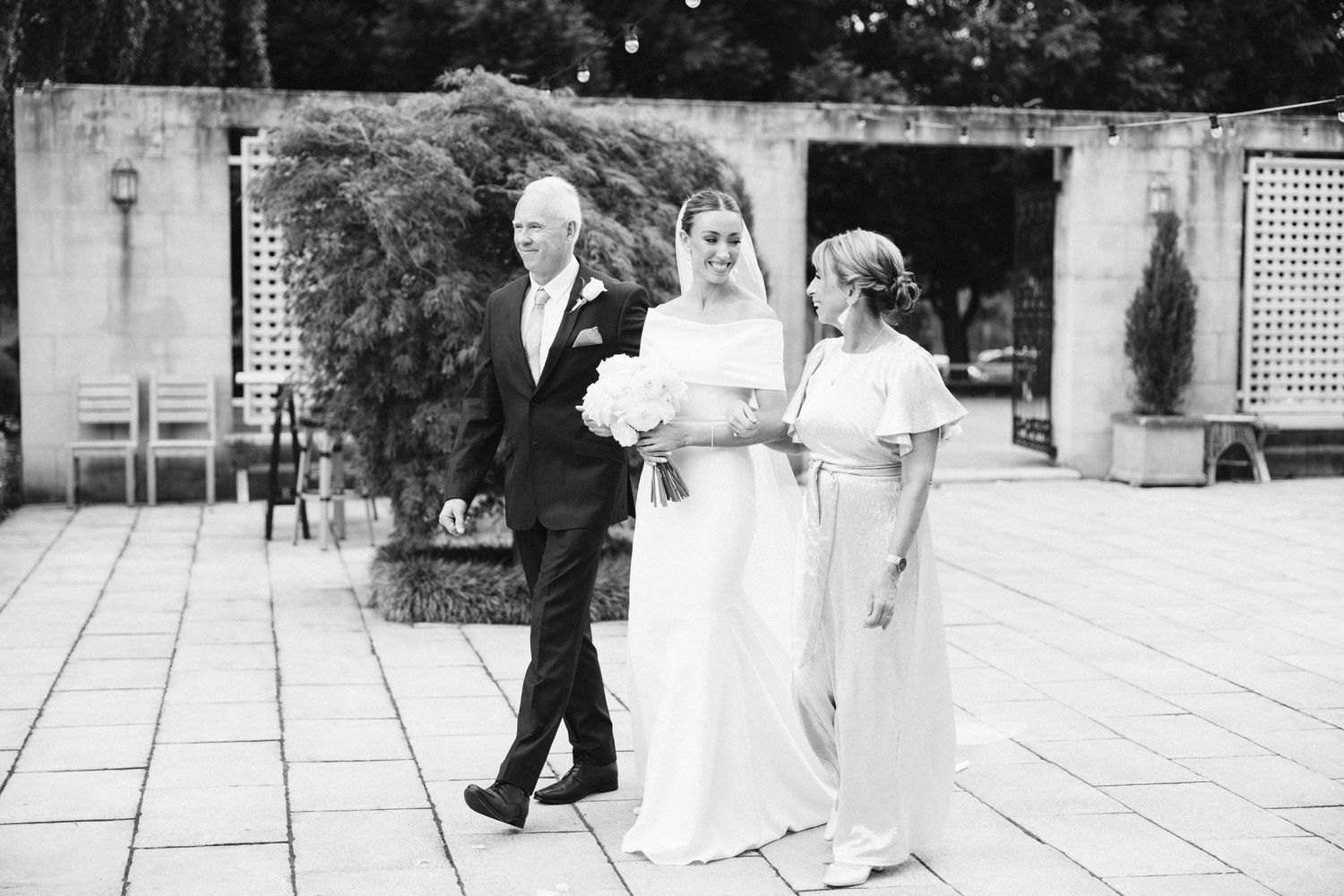 Black and white wedding processional photo on stone patio.
