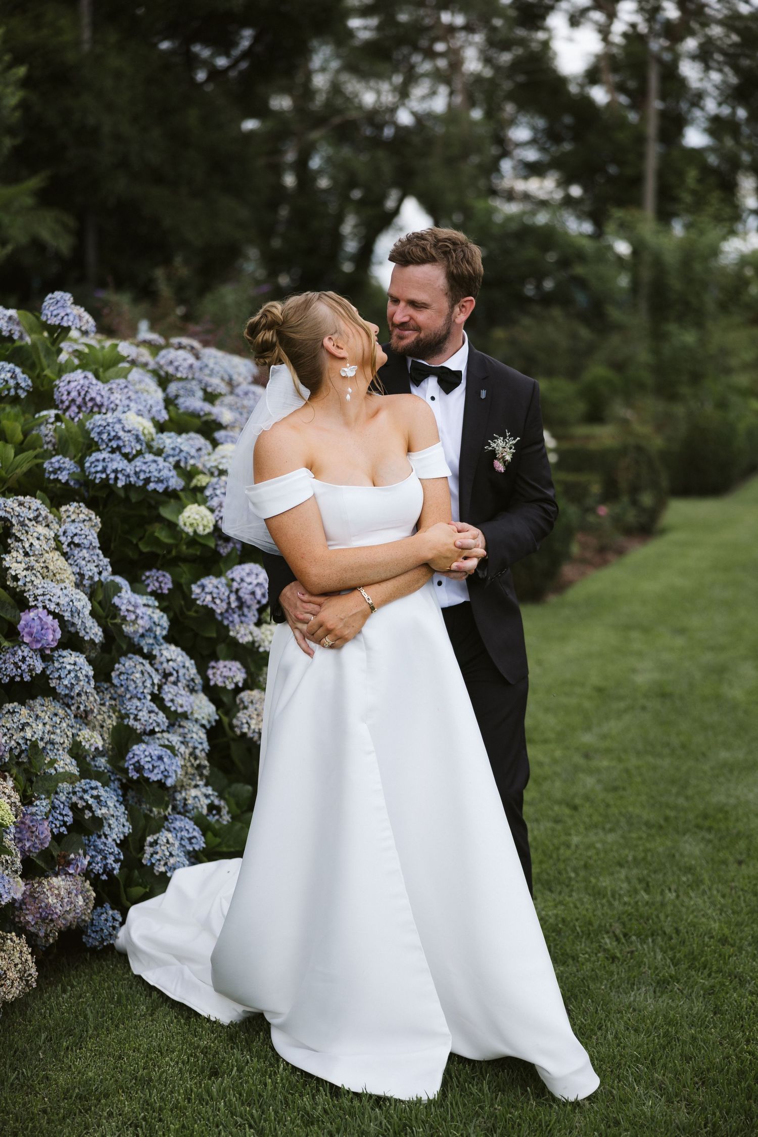 Romantic wedding couple embracing in a garden with blooming blue hydrangeas.