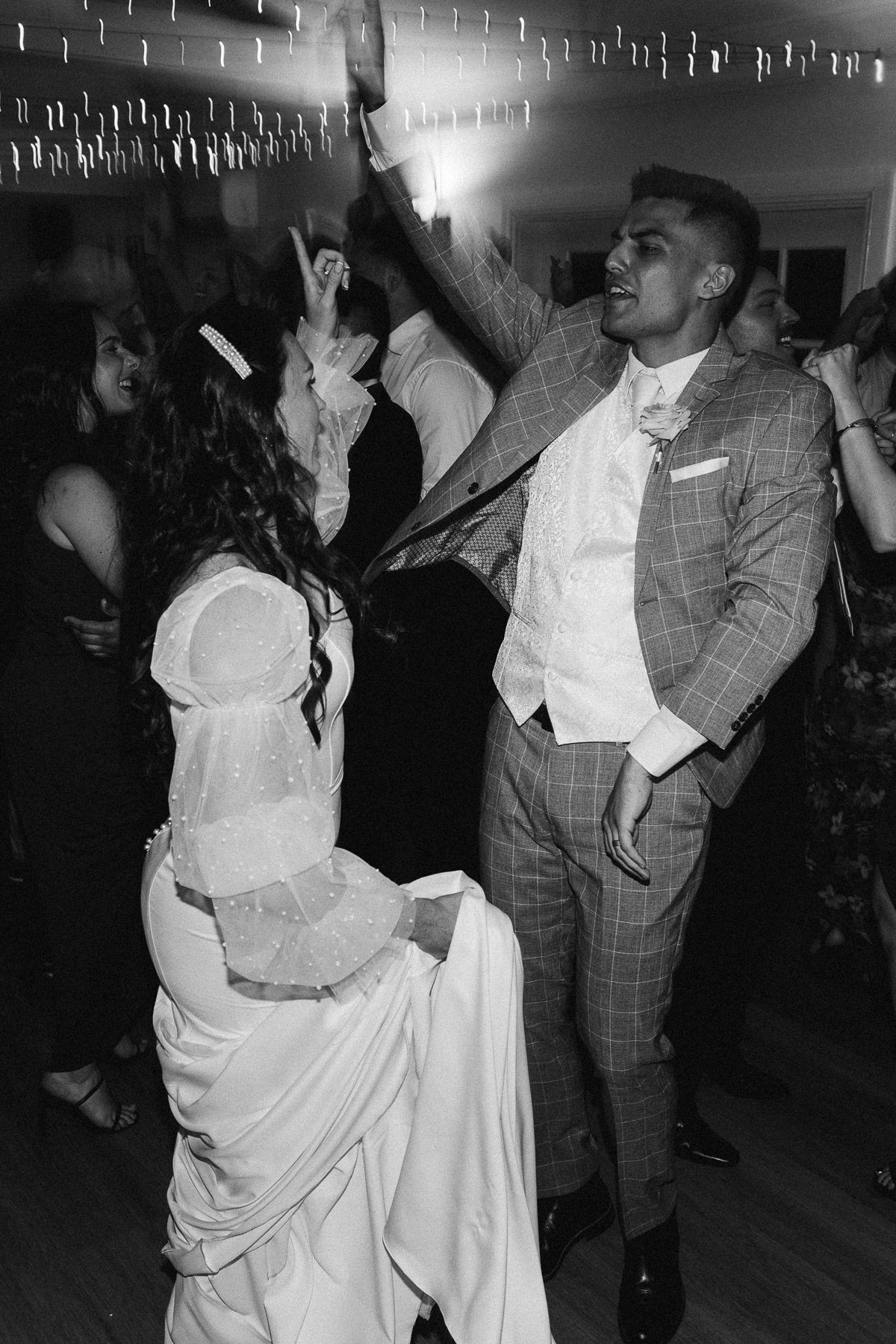 Black and white photo of bride and groom dancing joyfully at their wedding reception.