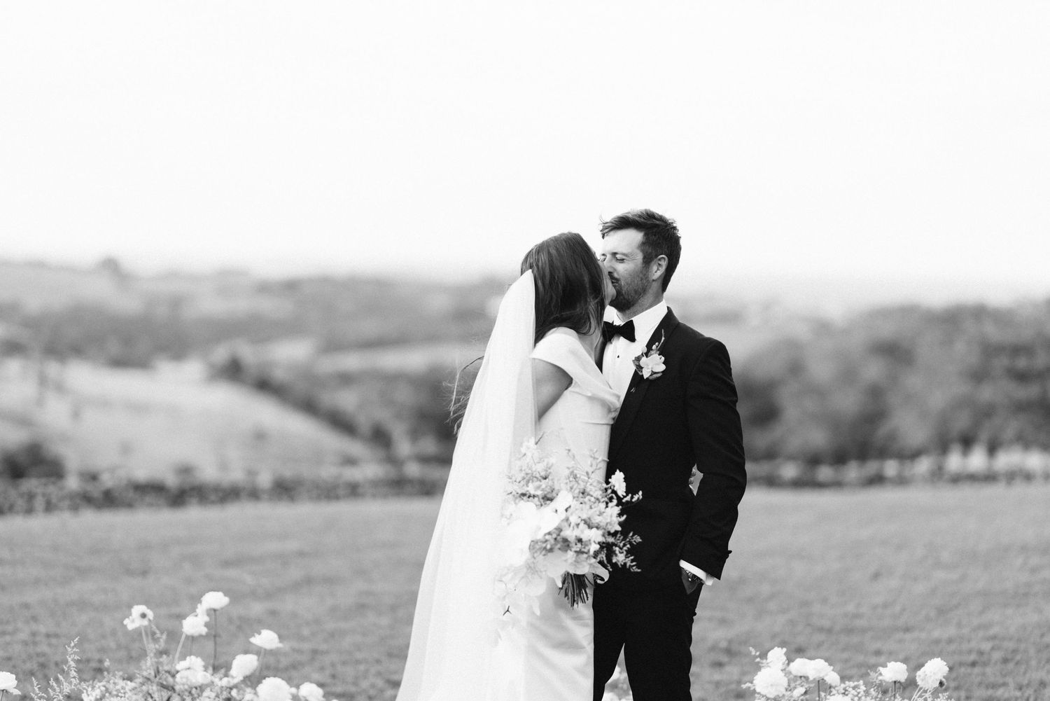 Black and white wedding portrait captured on hillside with scenic countryside views.