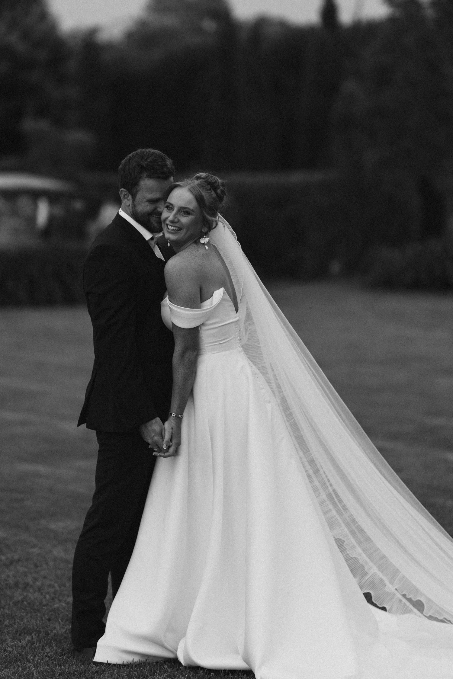 Romantic black and white portrait of newlyweds embracing on a manicured lawn.