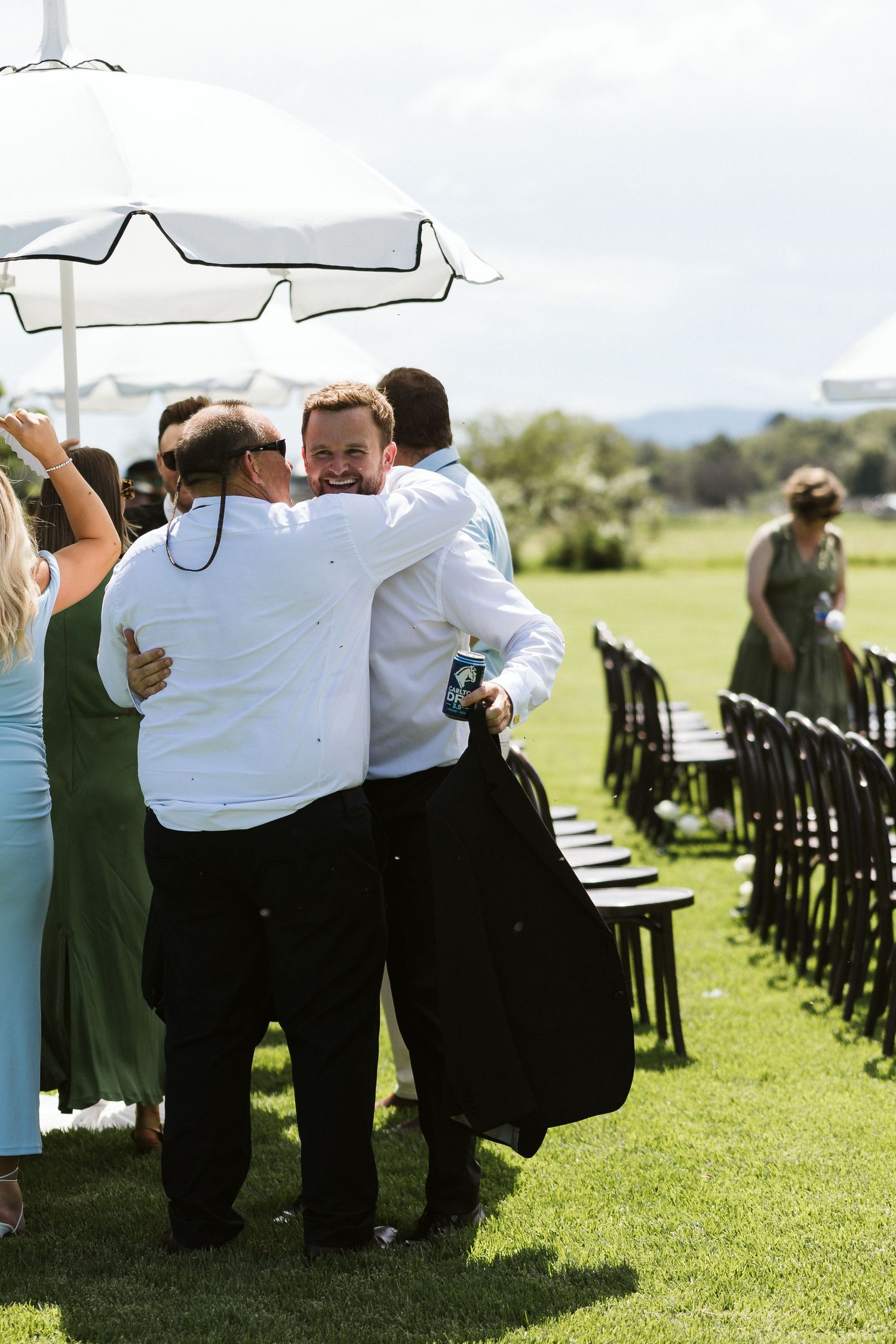 Group embracing during outdoor celebration under white umbrellas on manicured lawn.