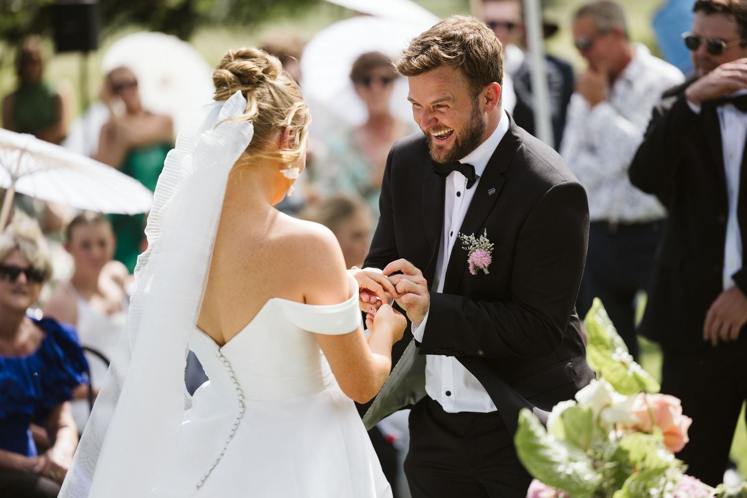 Sunny outdoor wedding ceremony with couple sharing a lighthearted moment.