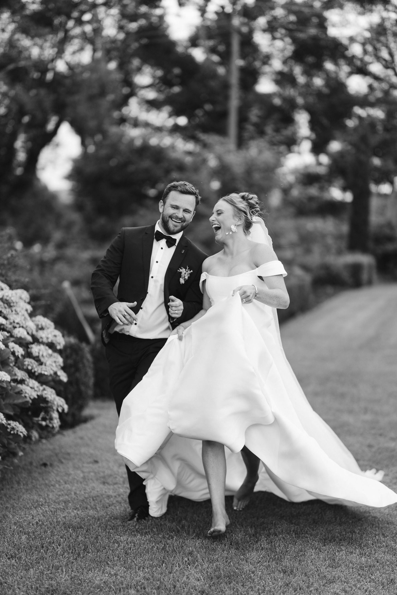 Black and white candid moment of newlyweds laughing together on garden path.