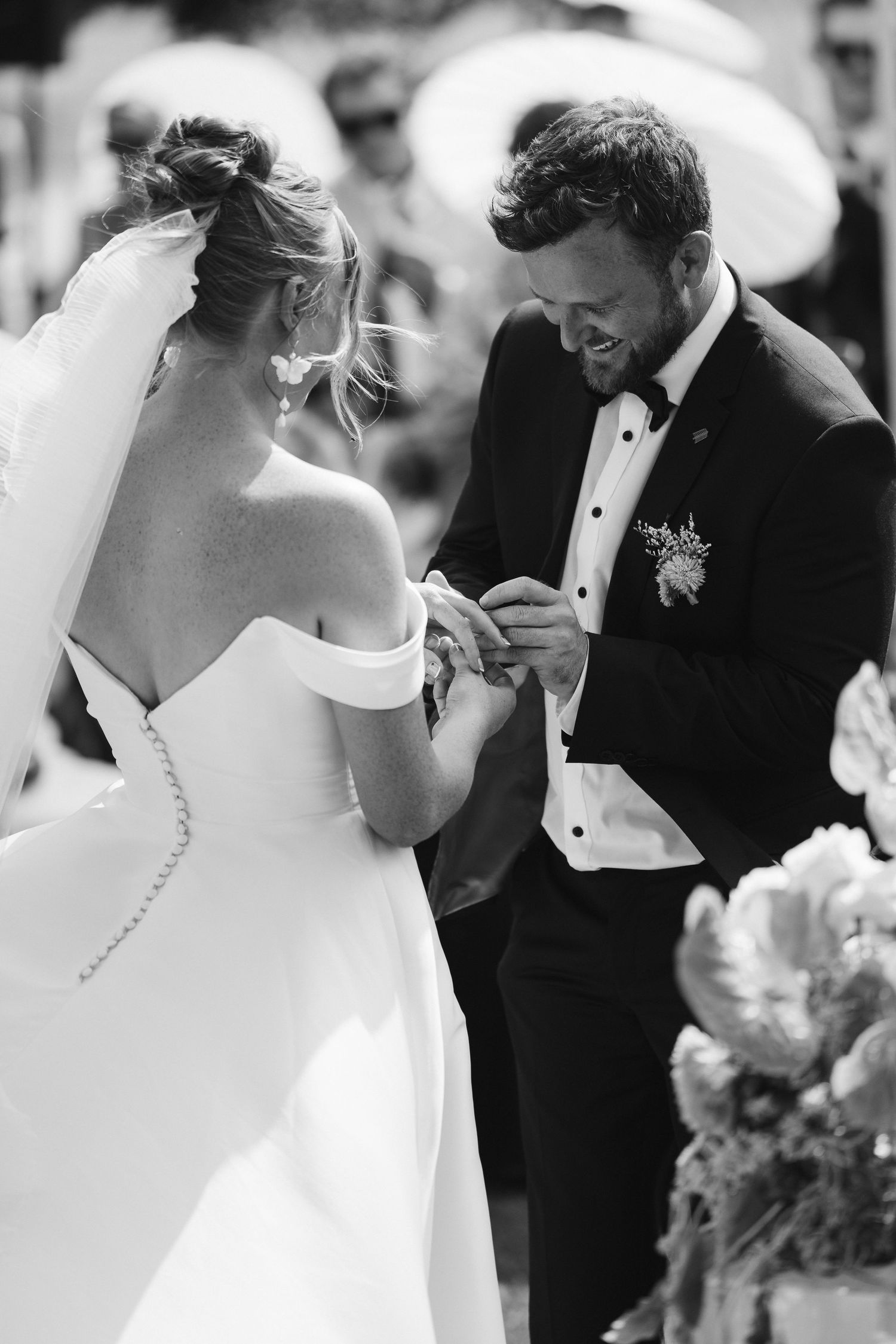 Black and white photo of wedding ring exchange during elegant outdoor ceremony.