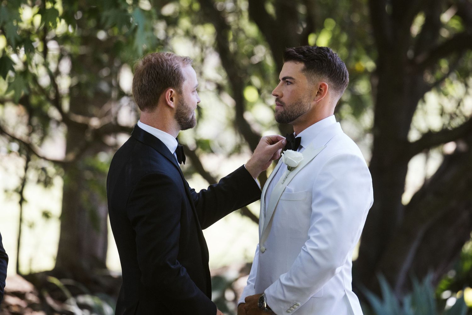 Best man adjusting groom's bowtie during pre-ceremony preparations.