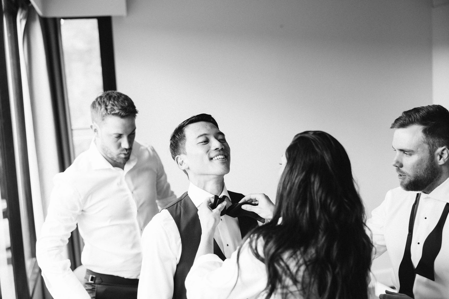Black and white photo of wedding preparations as formal attire is adjusted.
