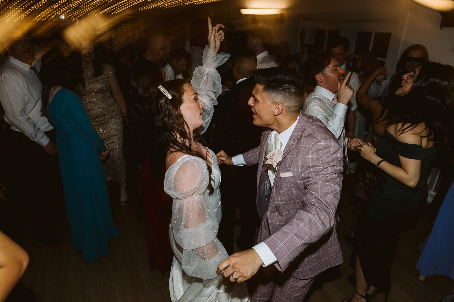 Couple dancing joyfully surrounded by guests at lively wedding reception.