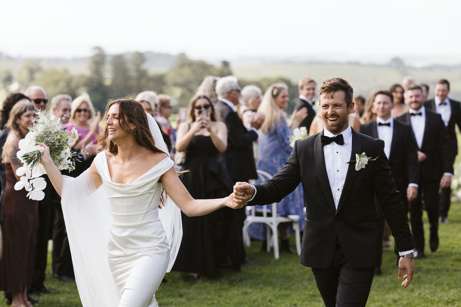 Newlyweds joyfully exit their ceremony while guests cheer in the background.