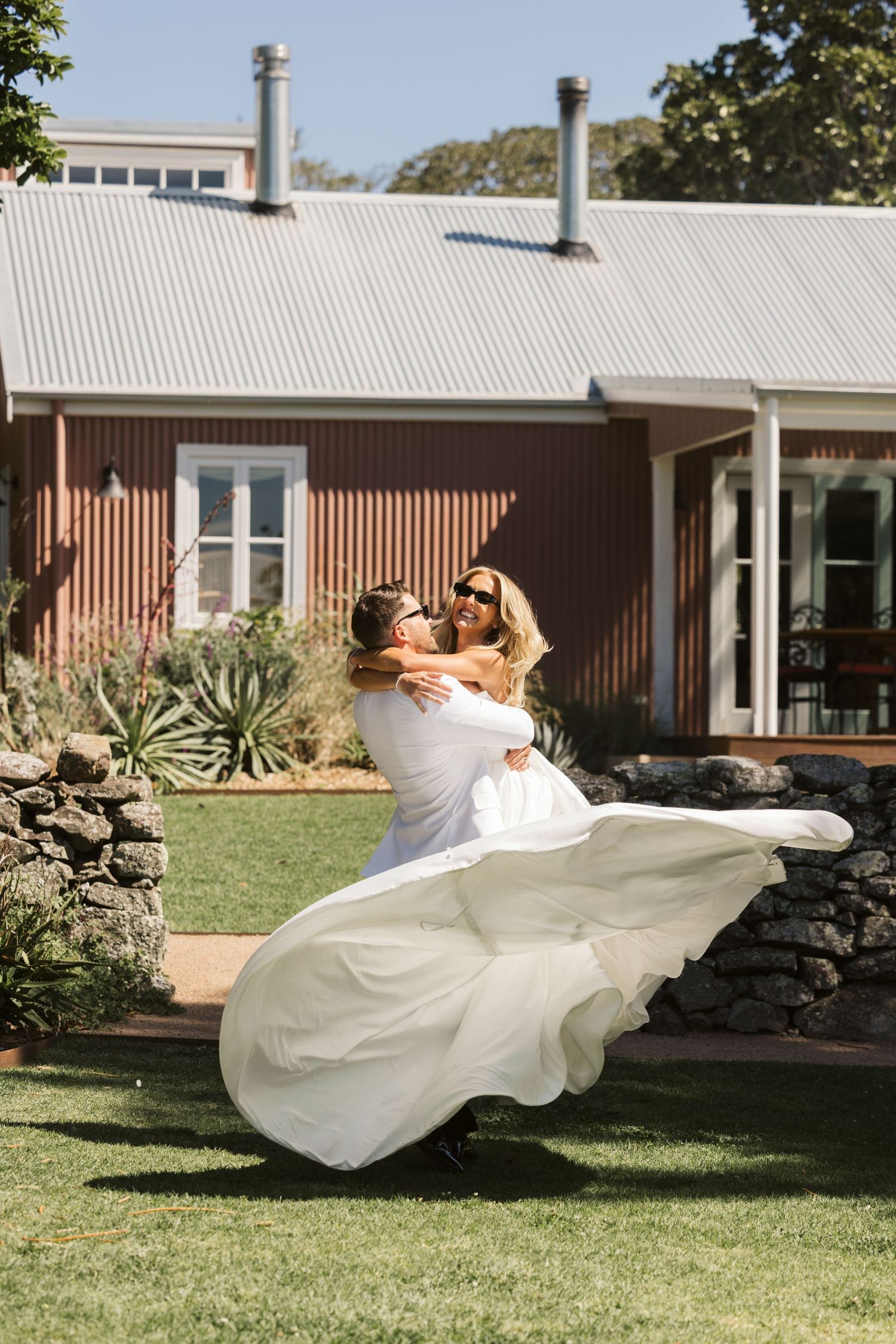 A romantic twirl between newlyweds on a lawn in front of a rustic brown building.