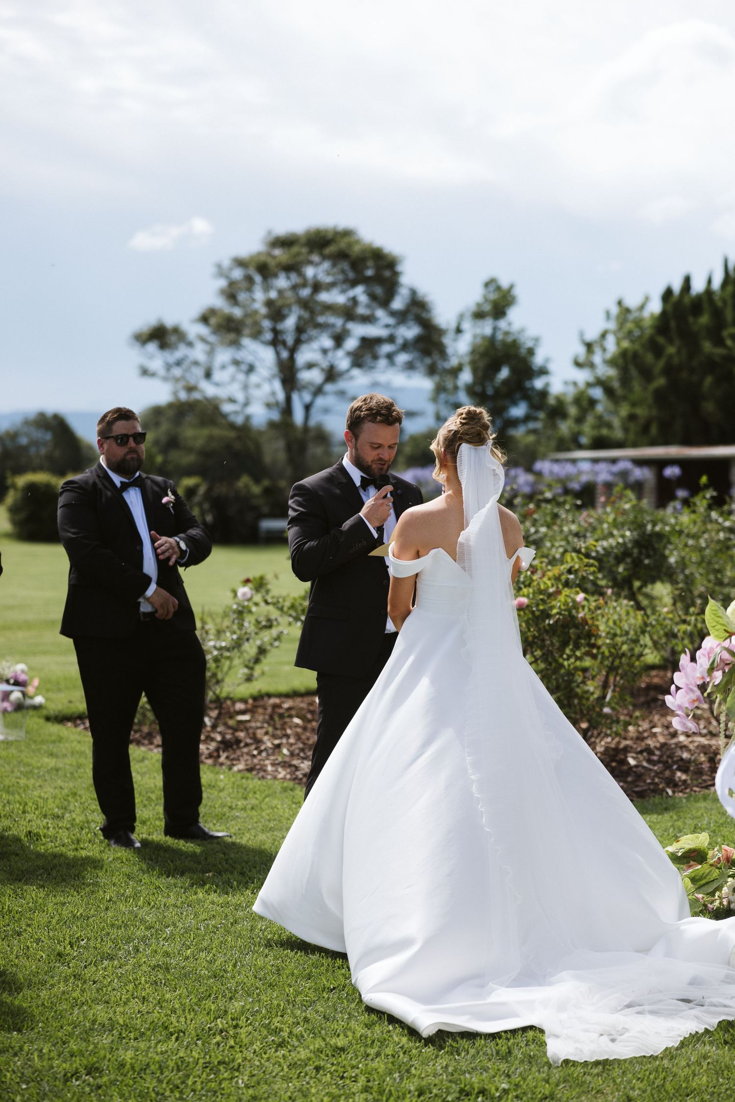 Elegant wedding ceremony in a manicured garden with tall cypress trees in the background.