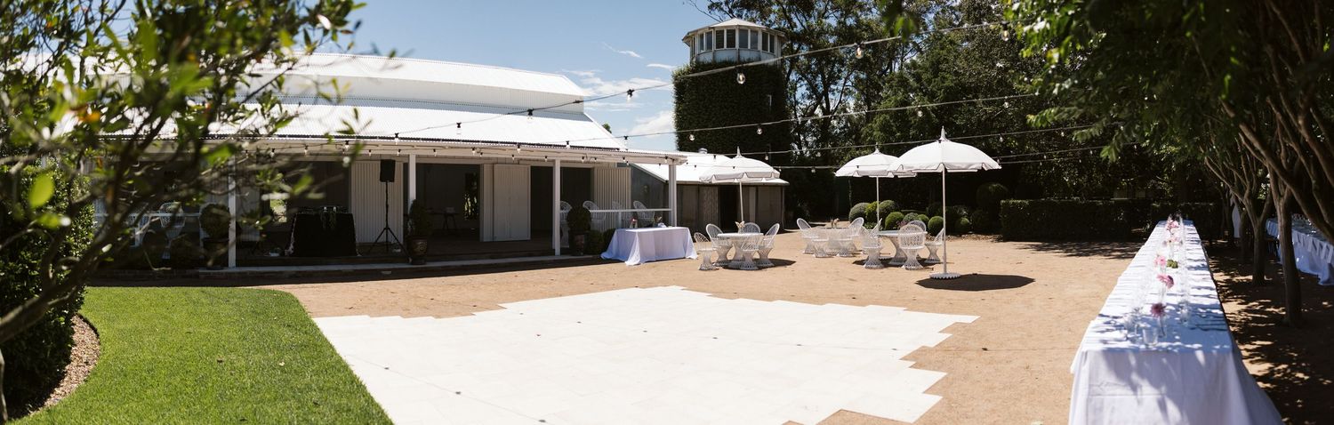 Elegant outdoor venue patio with white umbrellas and dining tables set up in a garden setting.