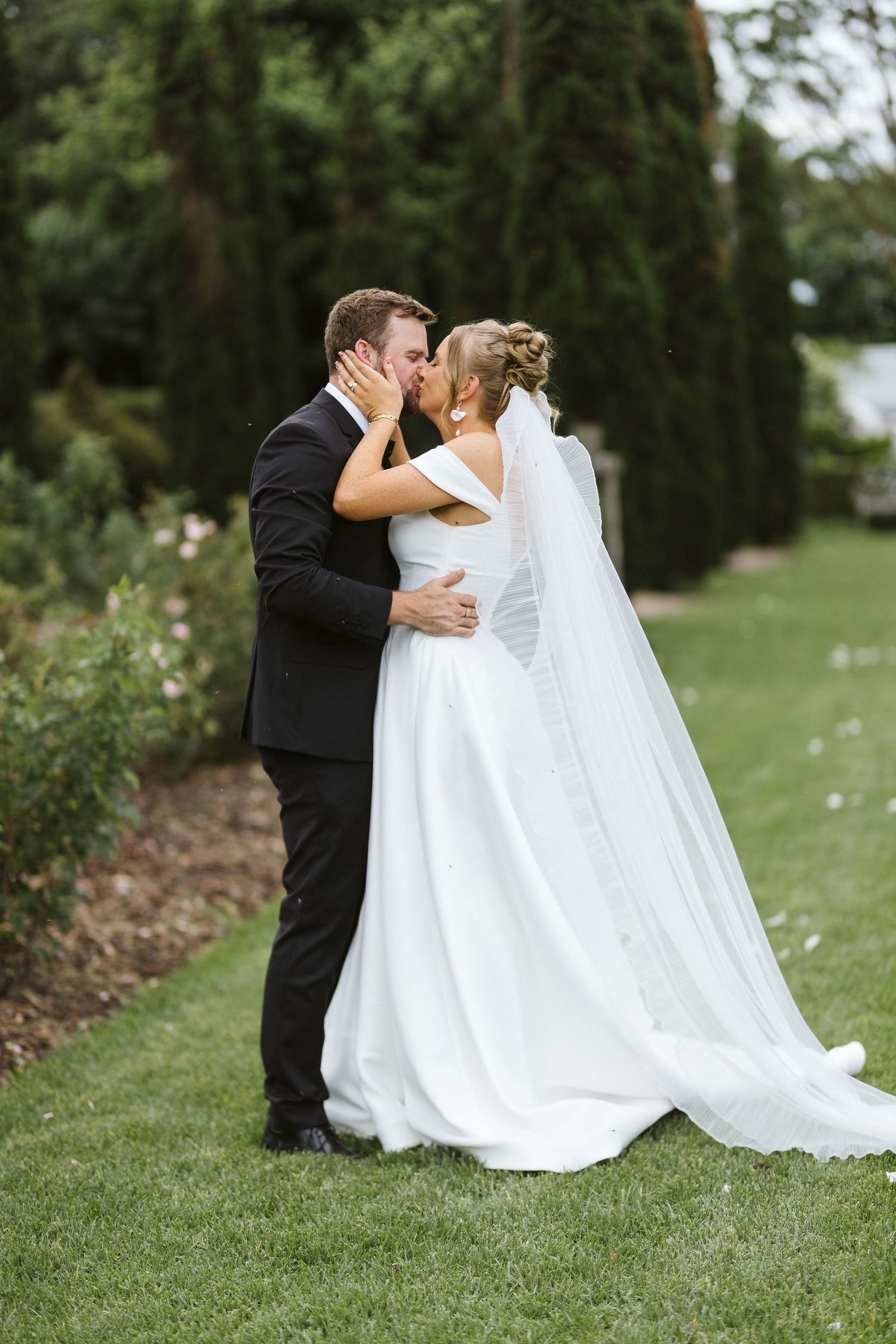 Intimate moment between newlyweds on a garden path with flowing veil.
