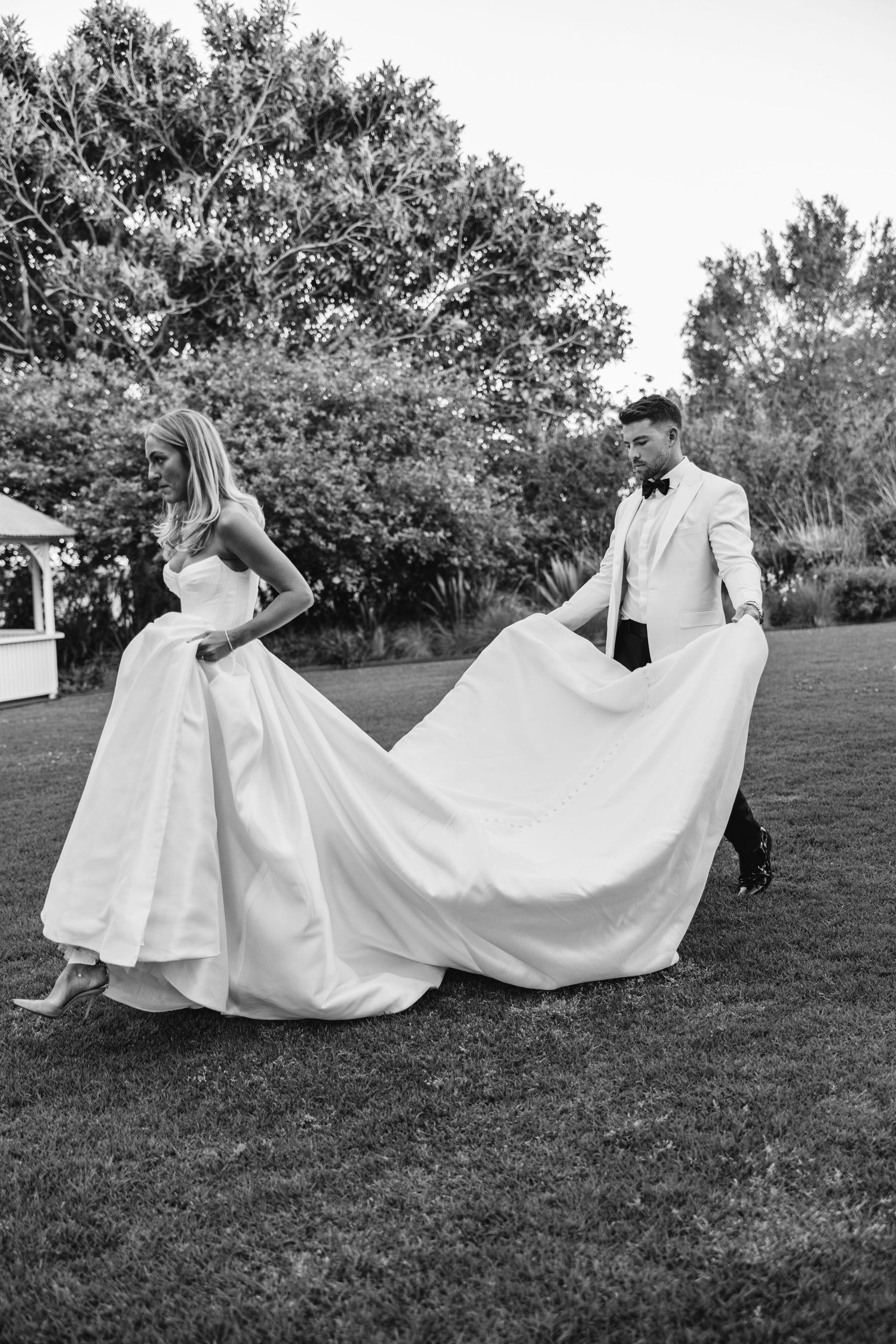 Black and white photo of couple playfully managing bride's flowing wedding dress train.