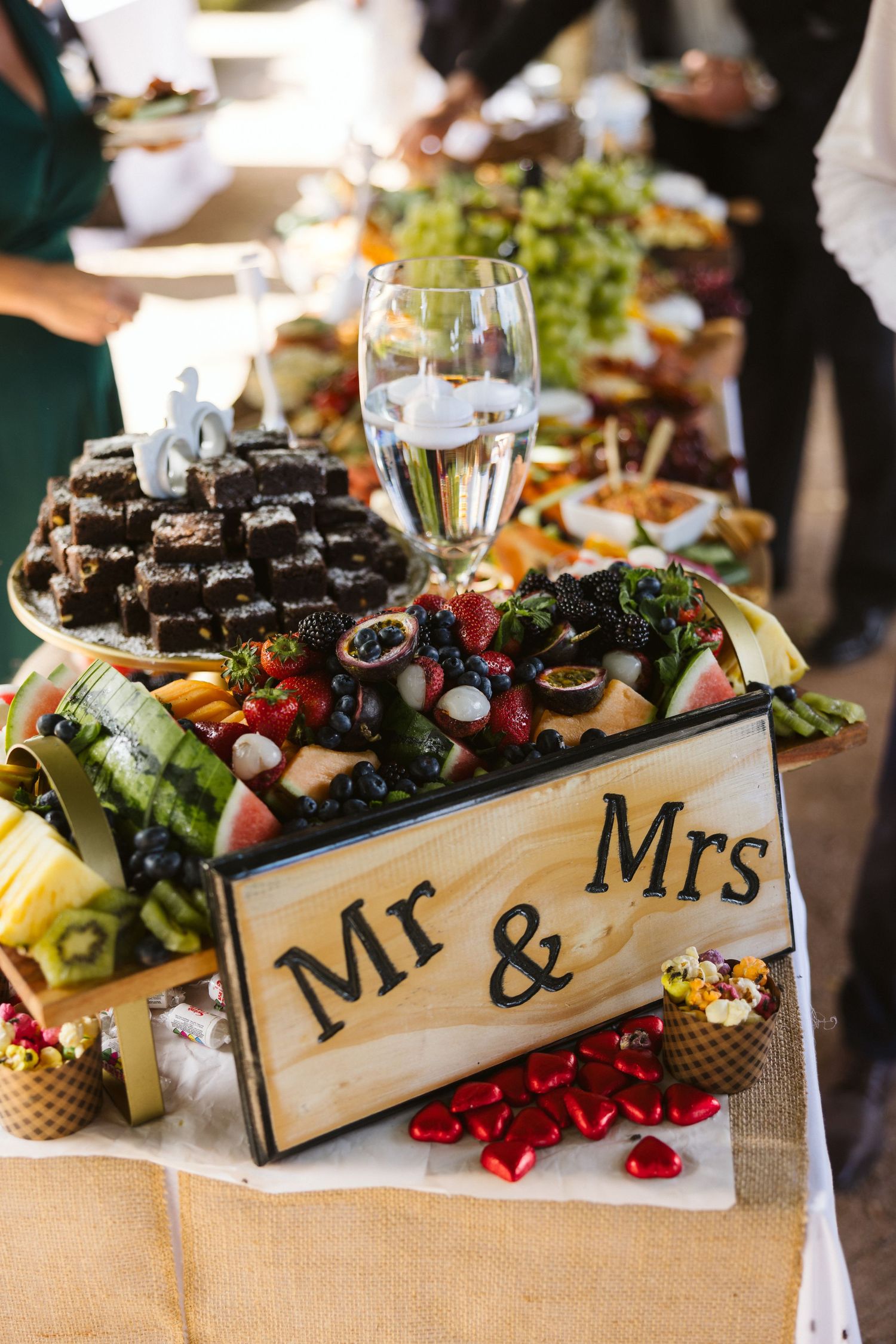 Wedding reception grazing table with a wooden Mr & Mrs sign, gourmet appetizers, and champagne glass.