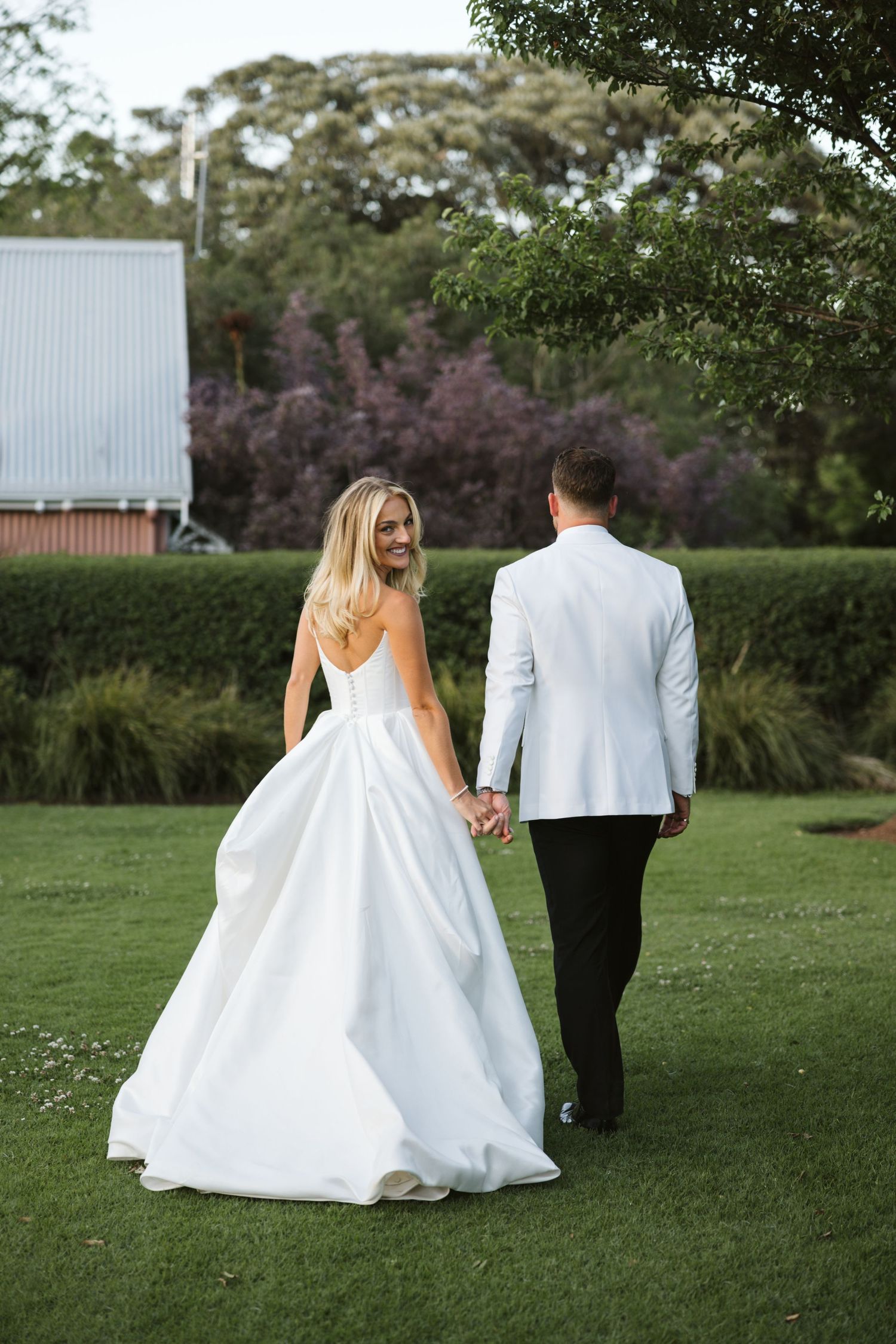 Bride and groom holding hands while walking on manicured lawn.
