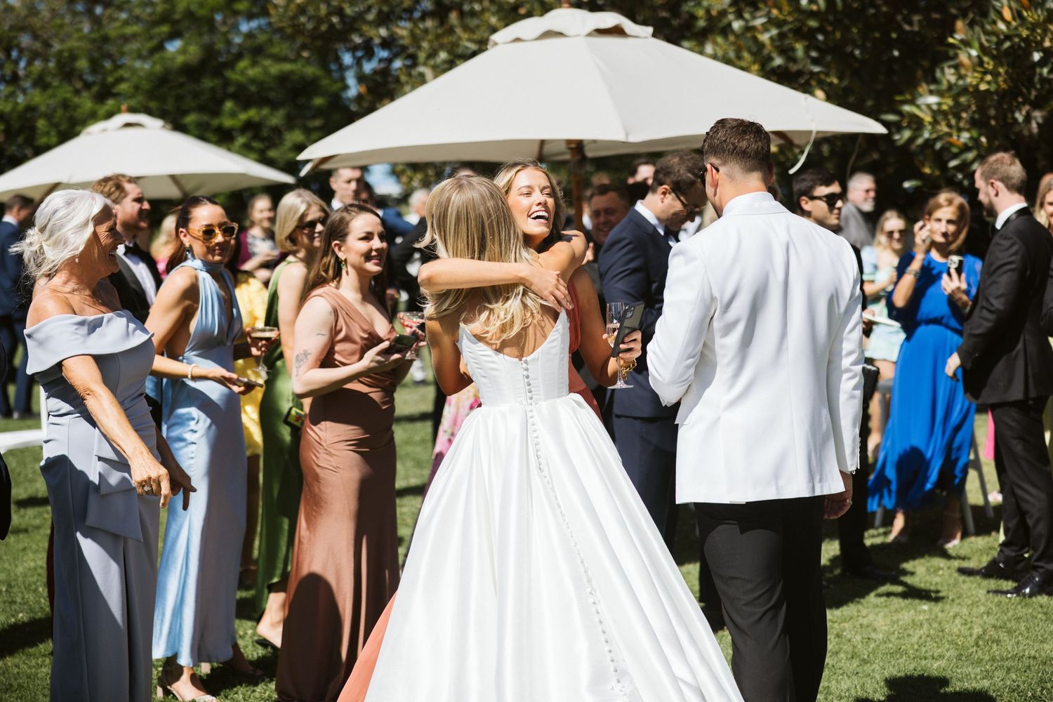 Wedding celebration on sunny lawn with white umbrellas and gathered guests.