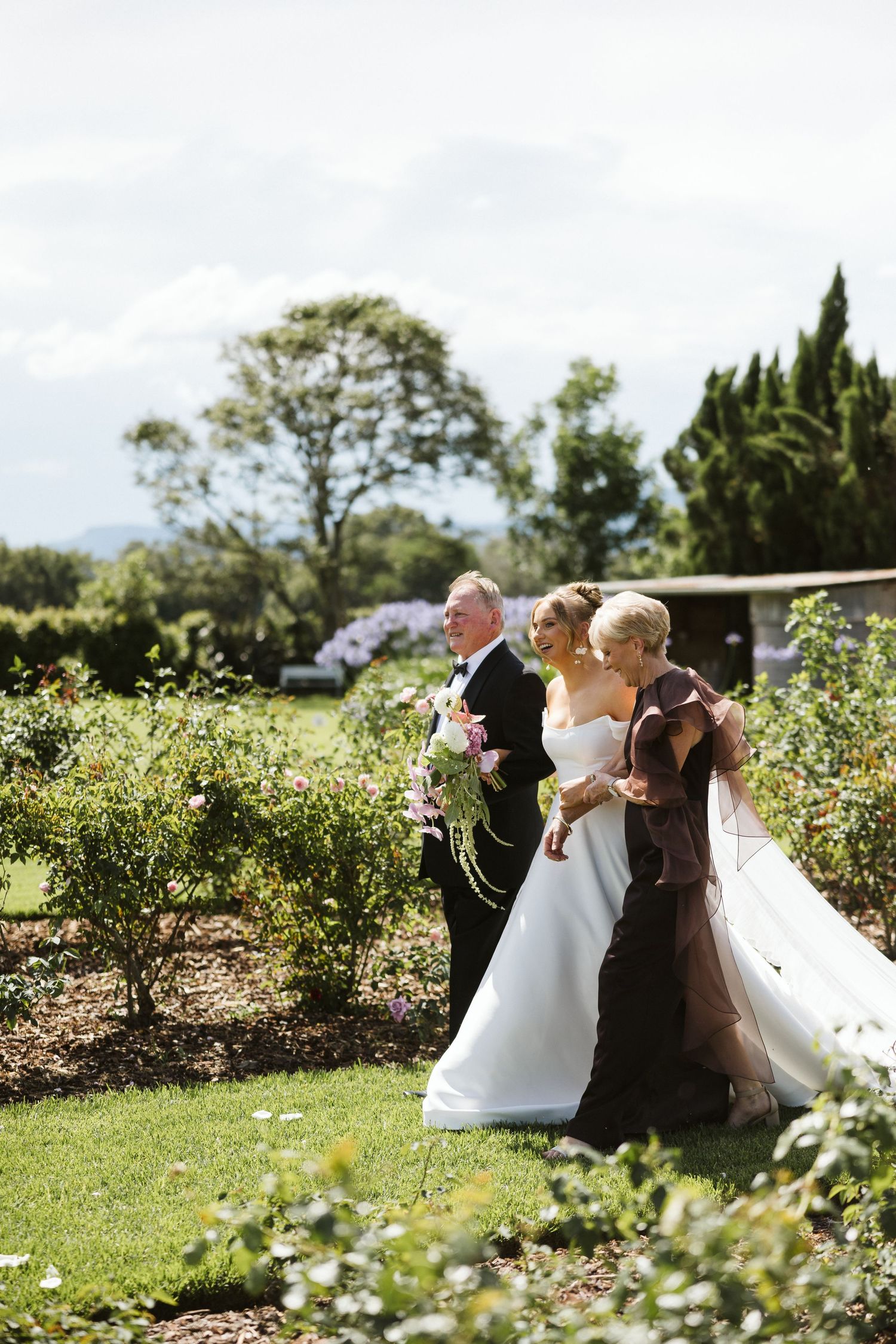A wedding party walking through a beautifully landscaped garden with cypress trees.