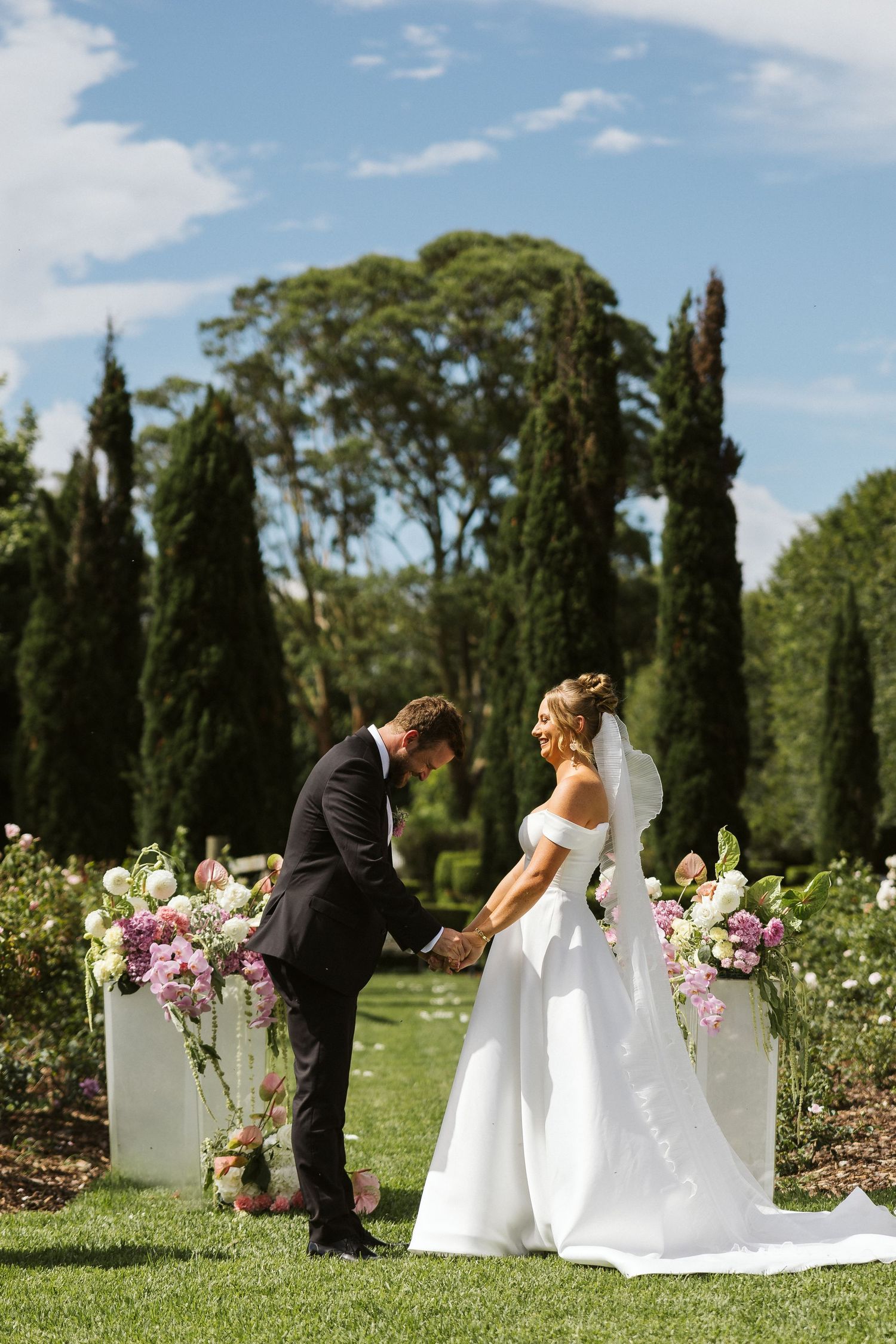 Elegant garden wedding ceremony with cypress trees and floral pedestals in a romantic outdoor setting.
