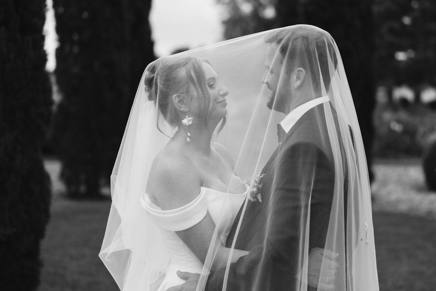 Intimate black and white wedding moment shared under a delicate veil in an outdoor garden setting.
