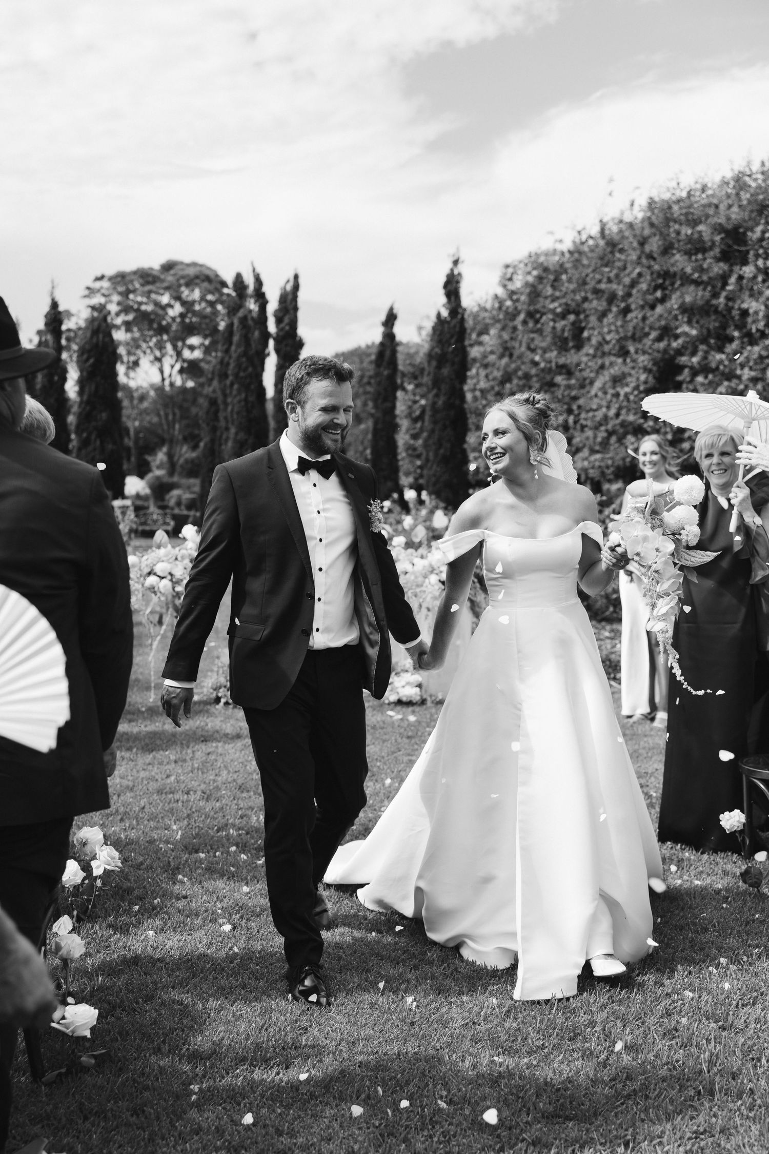 Wedding celebration on garden lawn with guests throwing confetti as couple walks together.