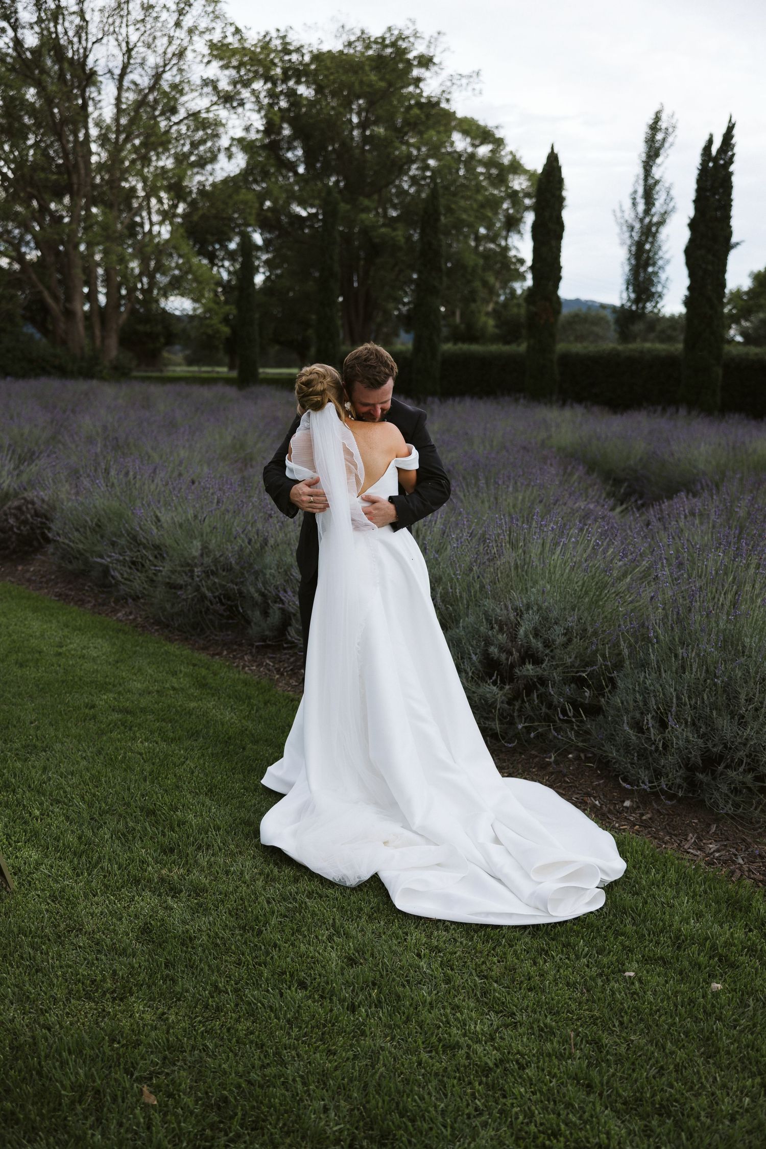 Couple shares intimate moment in lavender garden with bride's flowing white dress train.