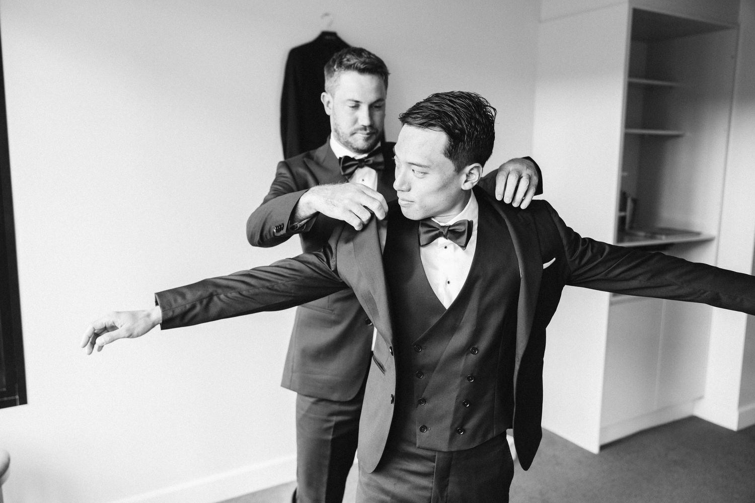 Two people in formal attire embrace playfully during wedding preparations.