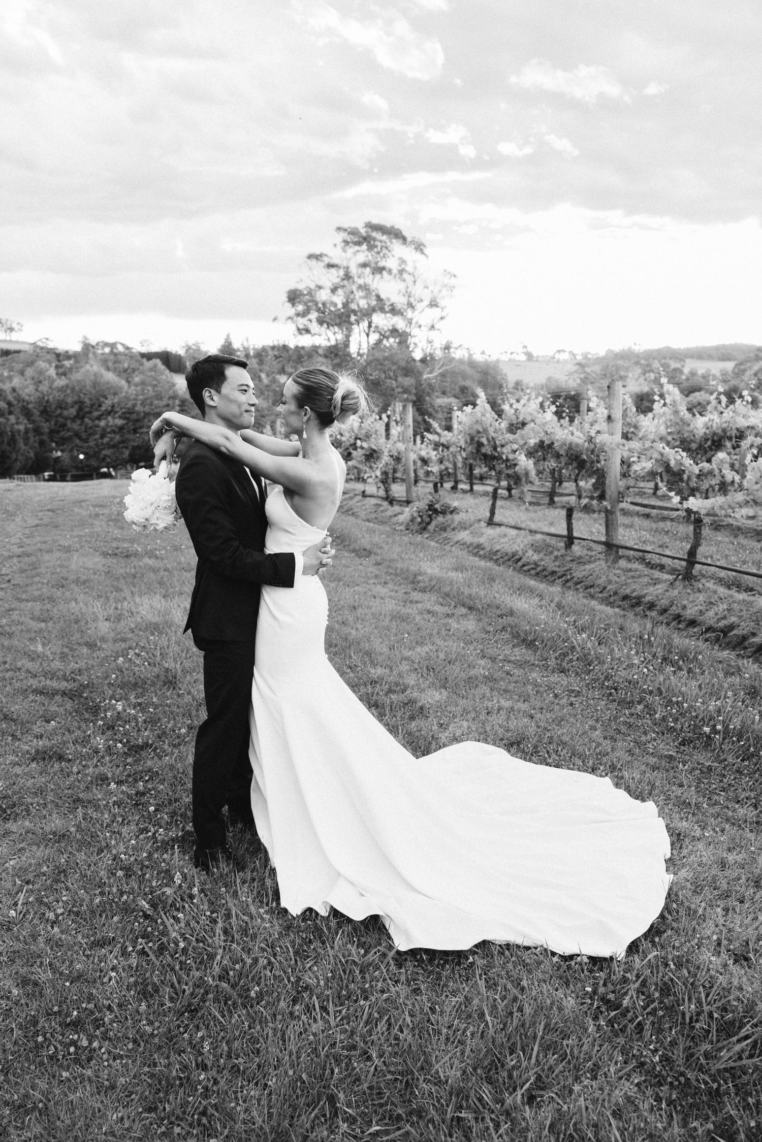 Black and white portrait of newlyweds dancing in vineyard with flowing wedding dress.