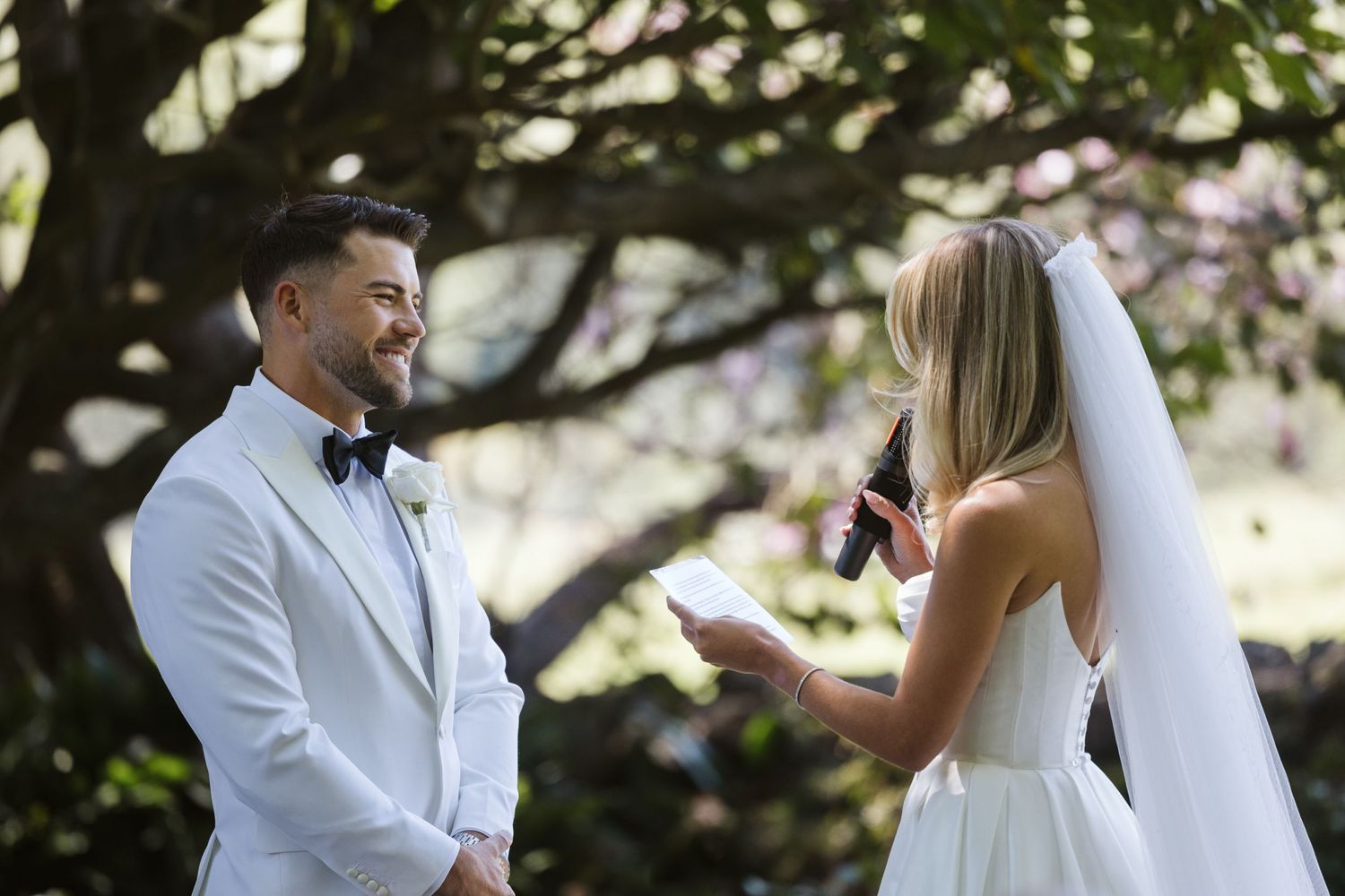 Couple exchanges wedding vows under shaded tree canopy.