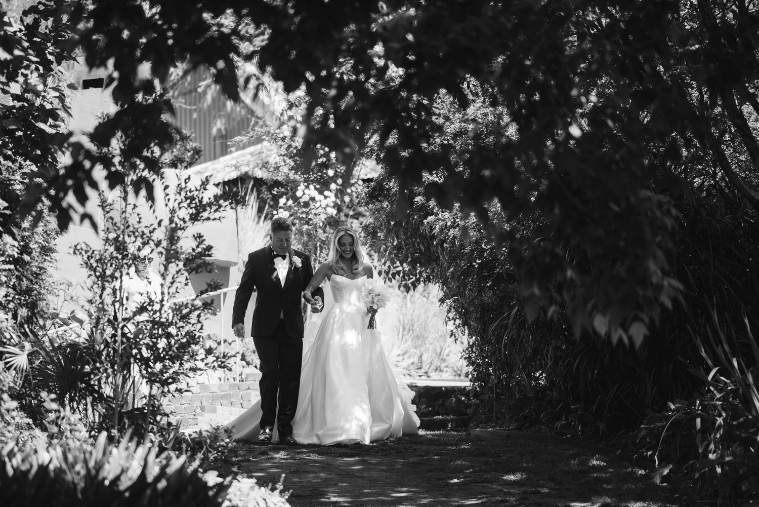 Black and white photo of couple walking through garden archway on wedding day.