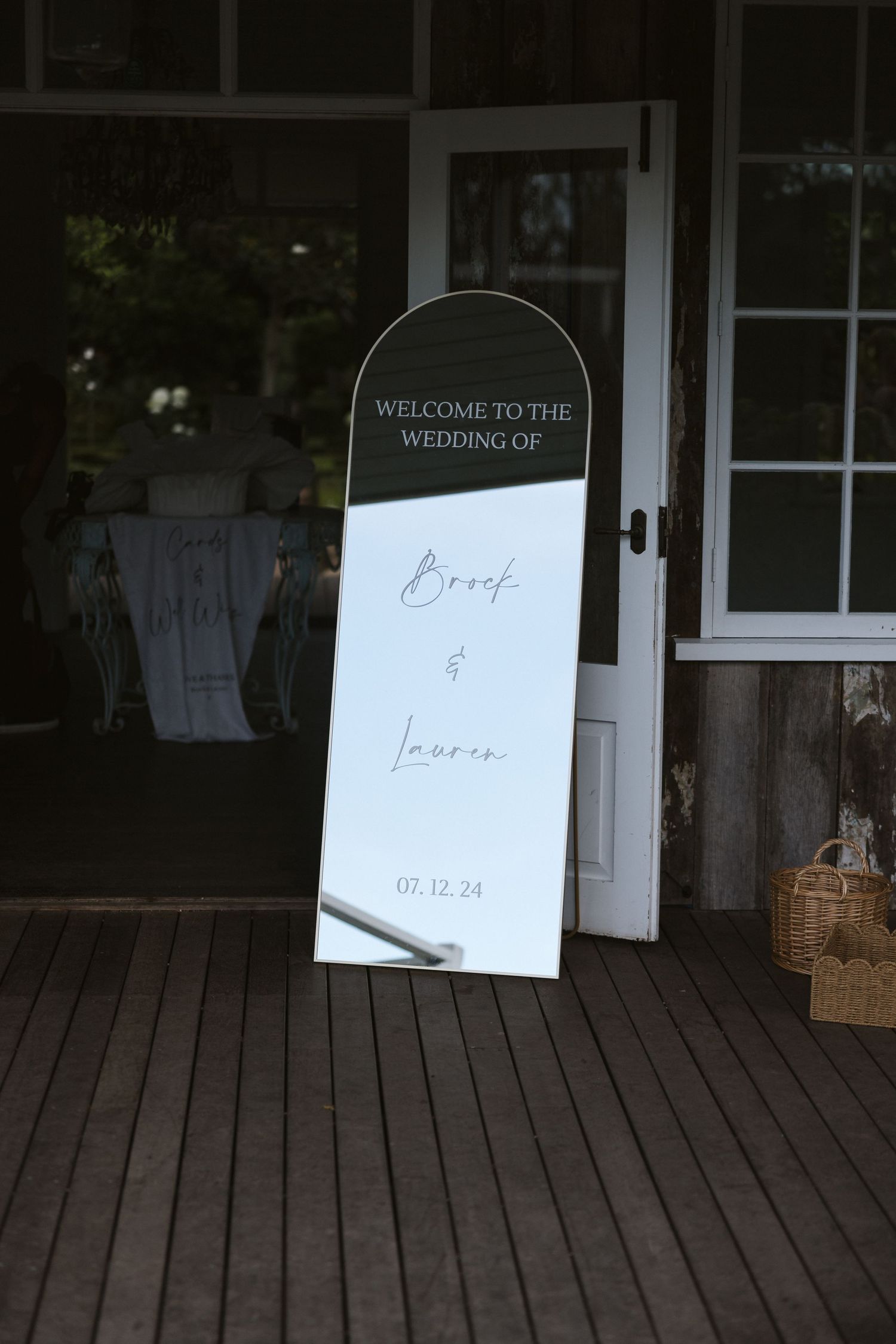 Elegant wedding welcome sign on wooden stand displayed on rustic porch deck.