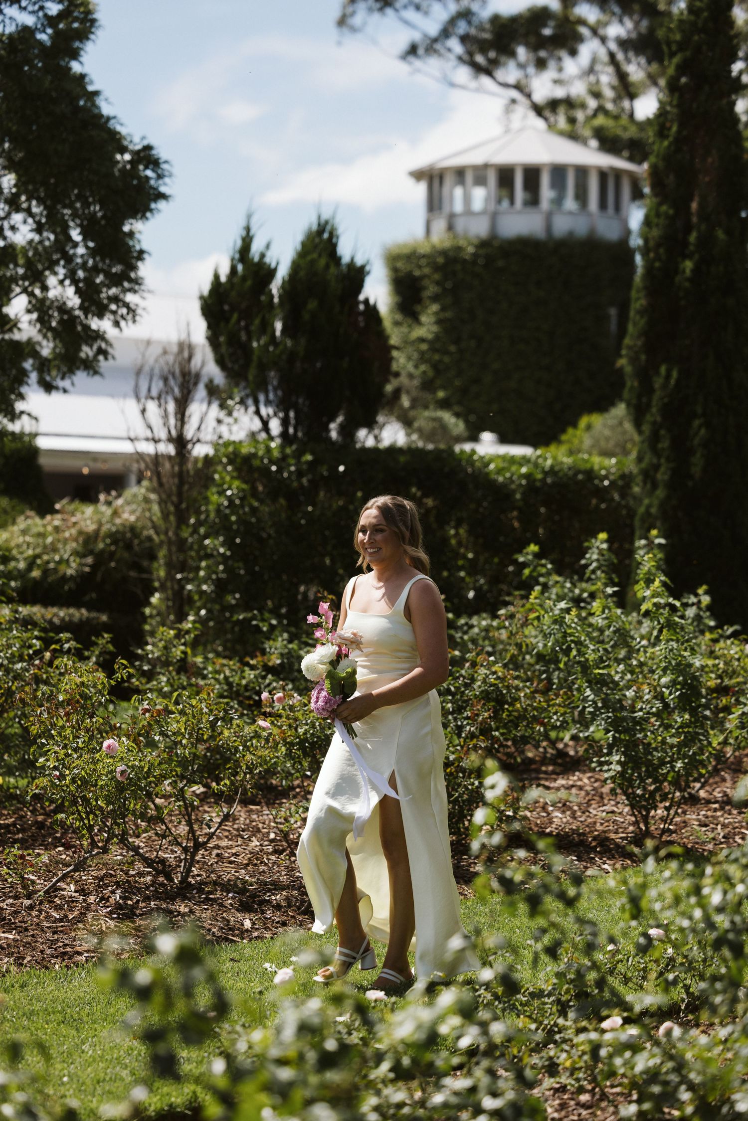 A sunny garden scene with tall cypress trees and a white gazebo in the background.
