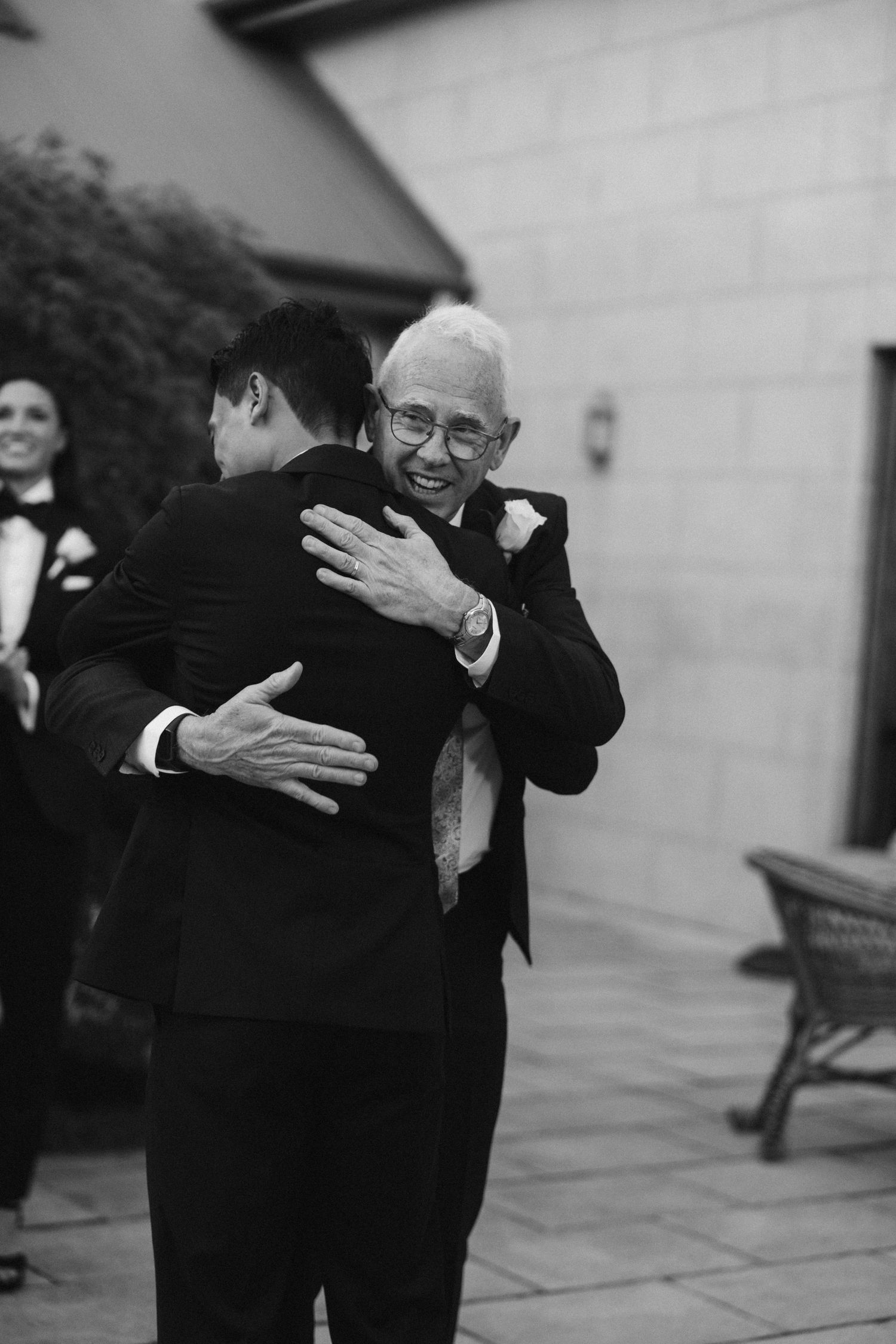 Black and white emotional moment of two men hugging during wedding celebration.