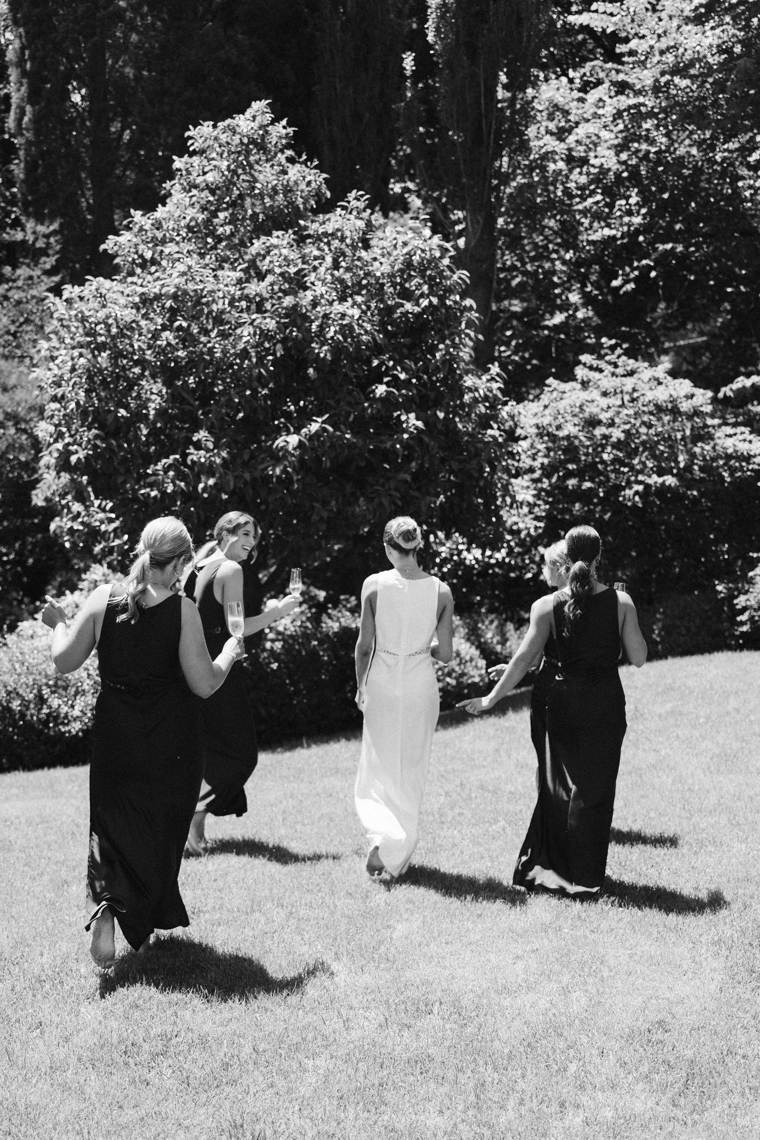 Black and white photo of wedding party walking through a garden together.